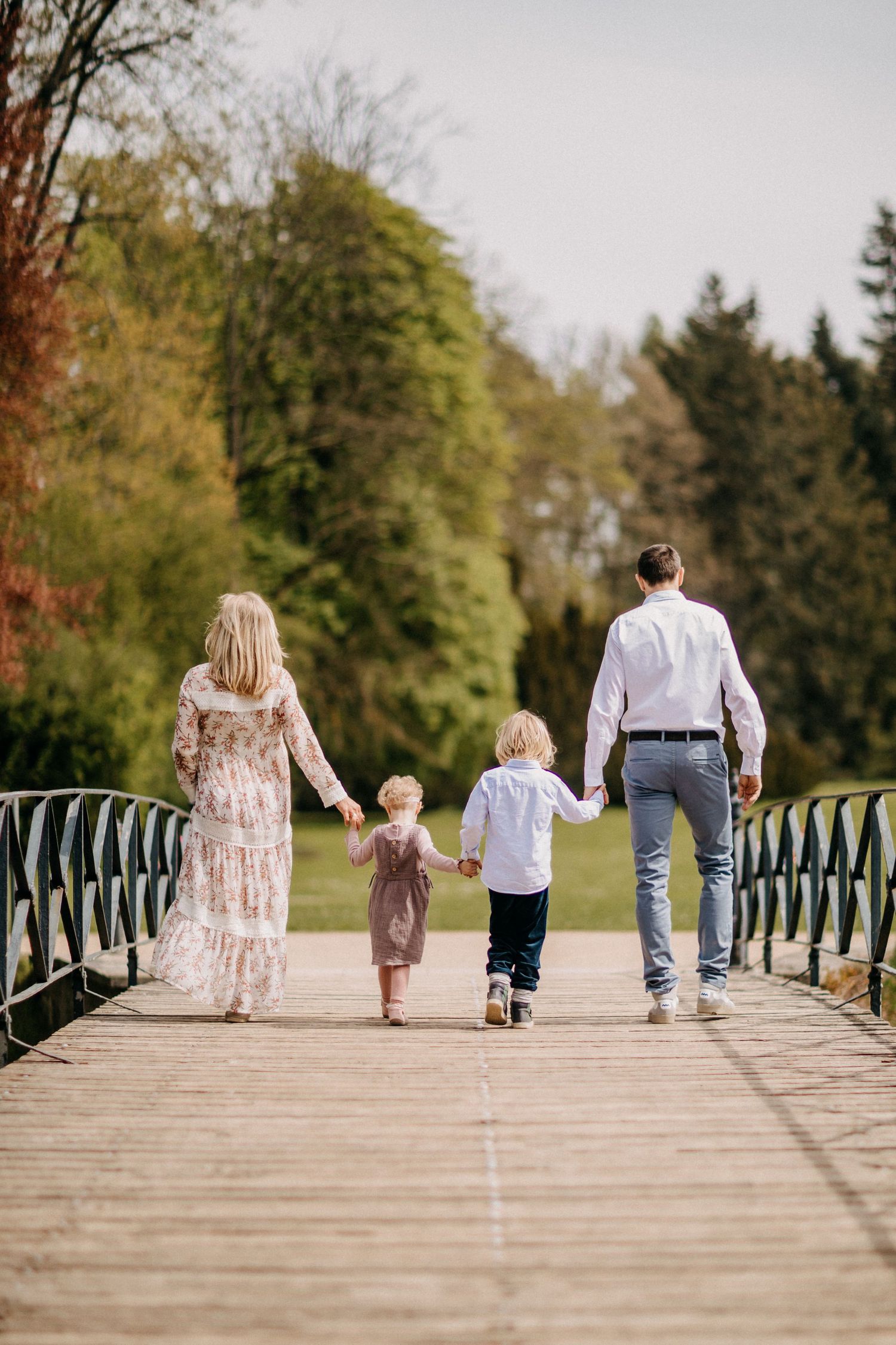 Eine Familie geht Hand in Hand über eine von Bäumen umgebene Holzbrücke.