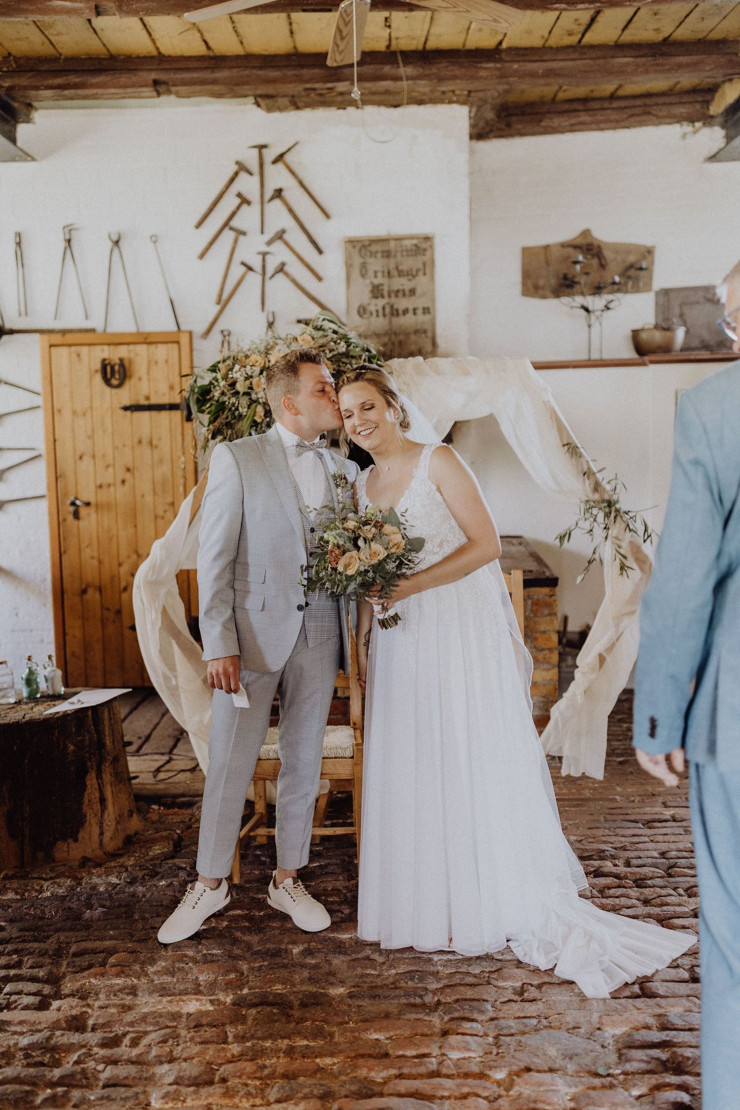 Hochzeitspaar posiert in rustikaler Innenumgebung mit Holzbalken und weißen Wänden.