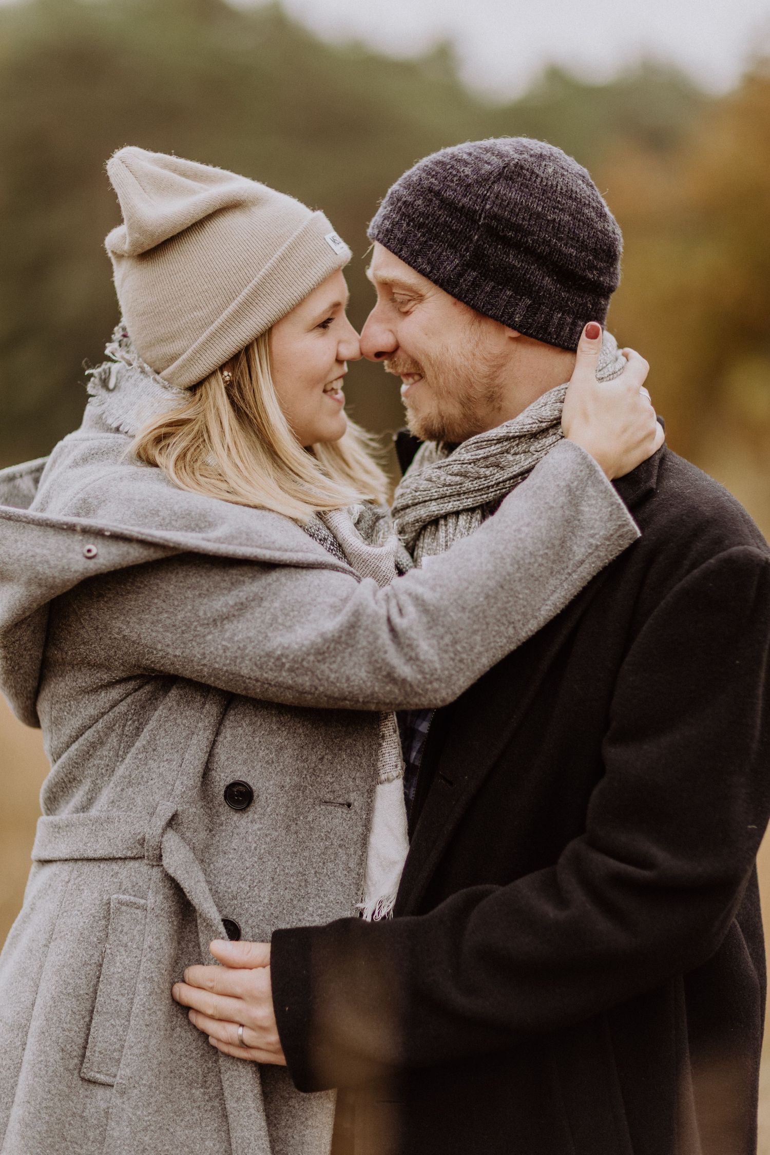 Ein Paar in Wintermänteln und Mützen teilt sich im Herbst einen intimen Moment im Freien.