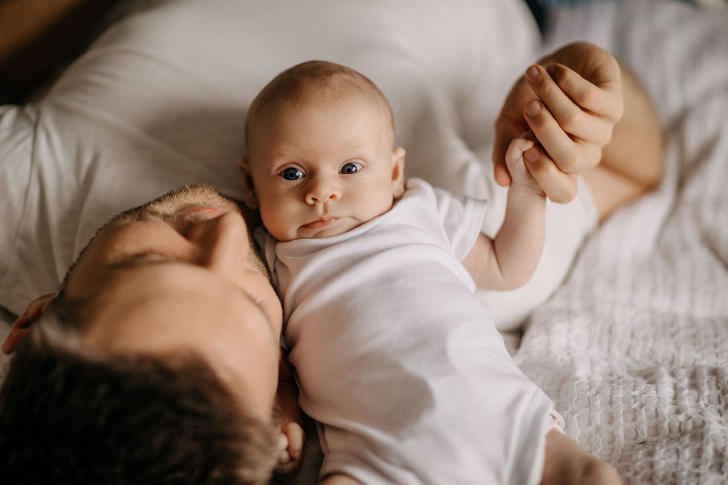 Nahaufnahmeporträt von Baby und Papa, die zarten Moment auf weißem Bettzeug teilen.