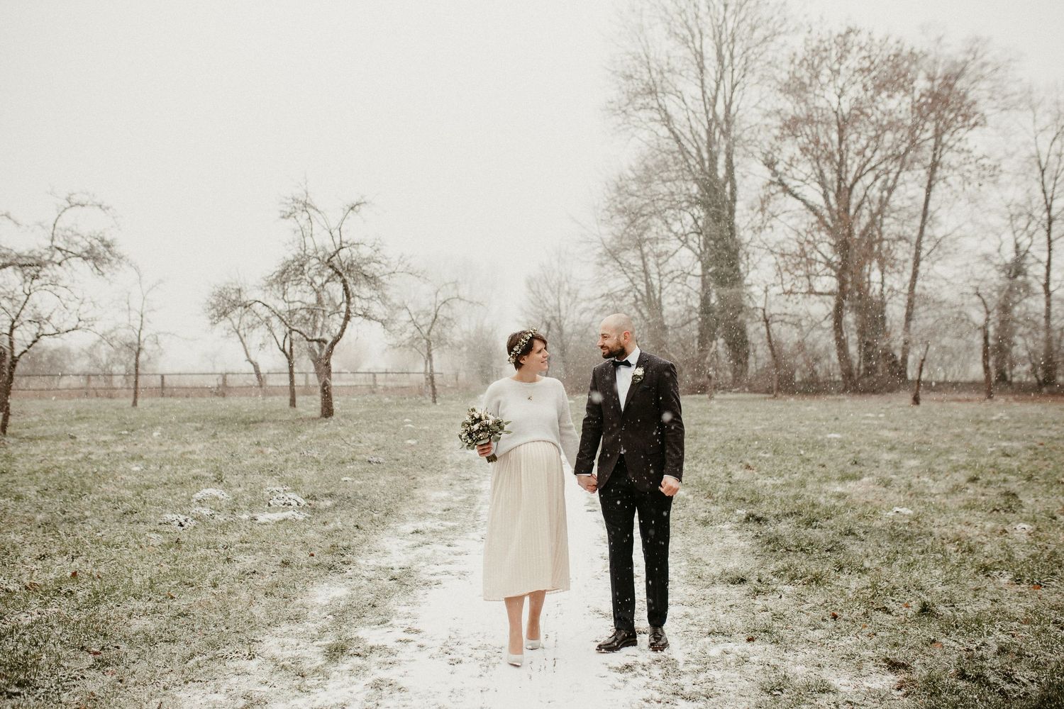 Hochzeitspaar steht zusammen in einem nebligen Winterfeld mit kahlen Bäumen.