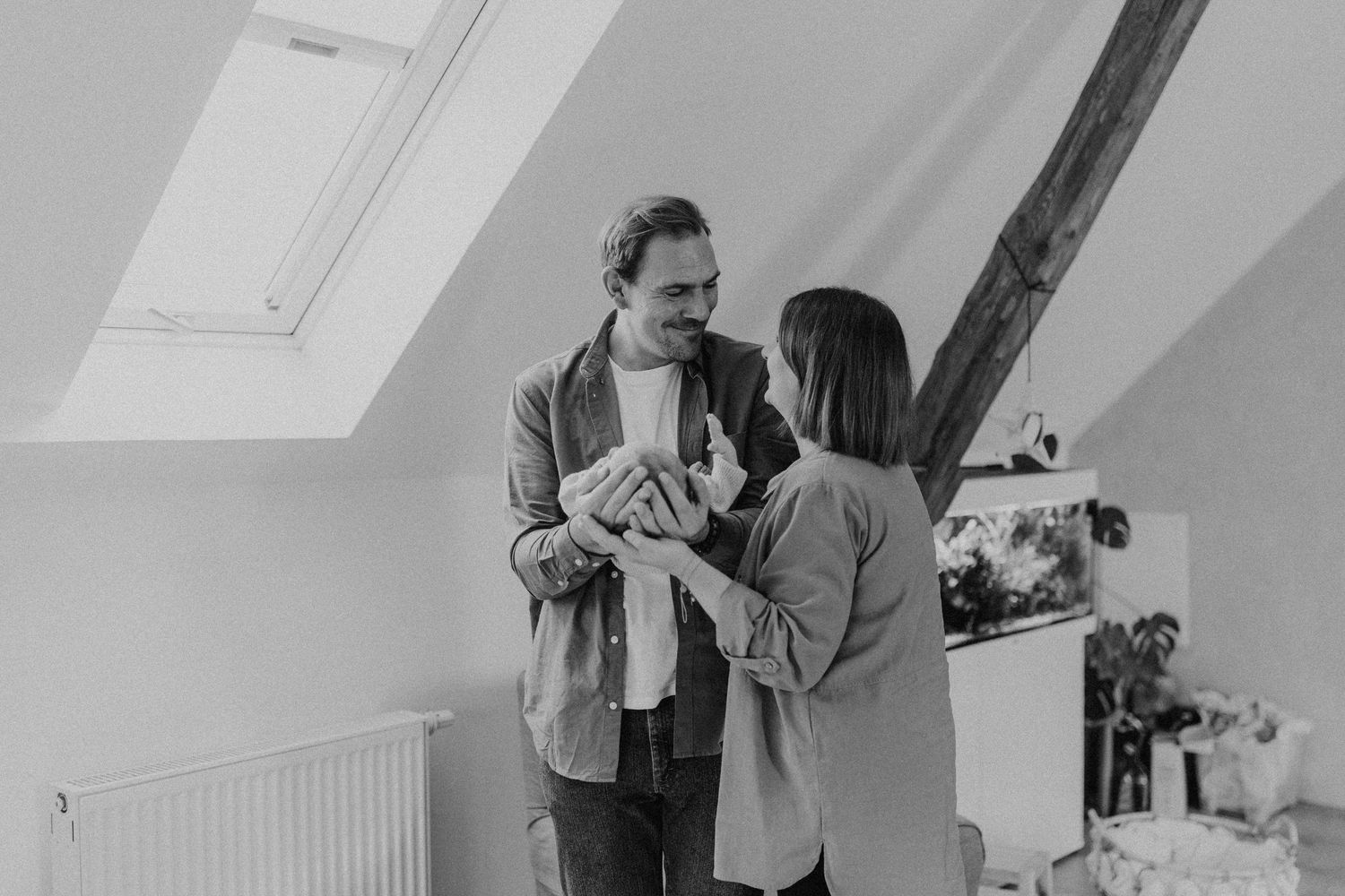 Paar teilt einen intimen Moment, während es ihr neugeborenes Baby in einem Dachzimmer hält.