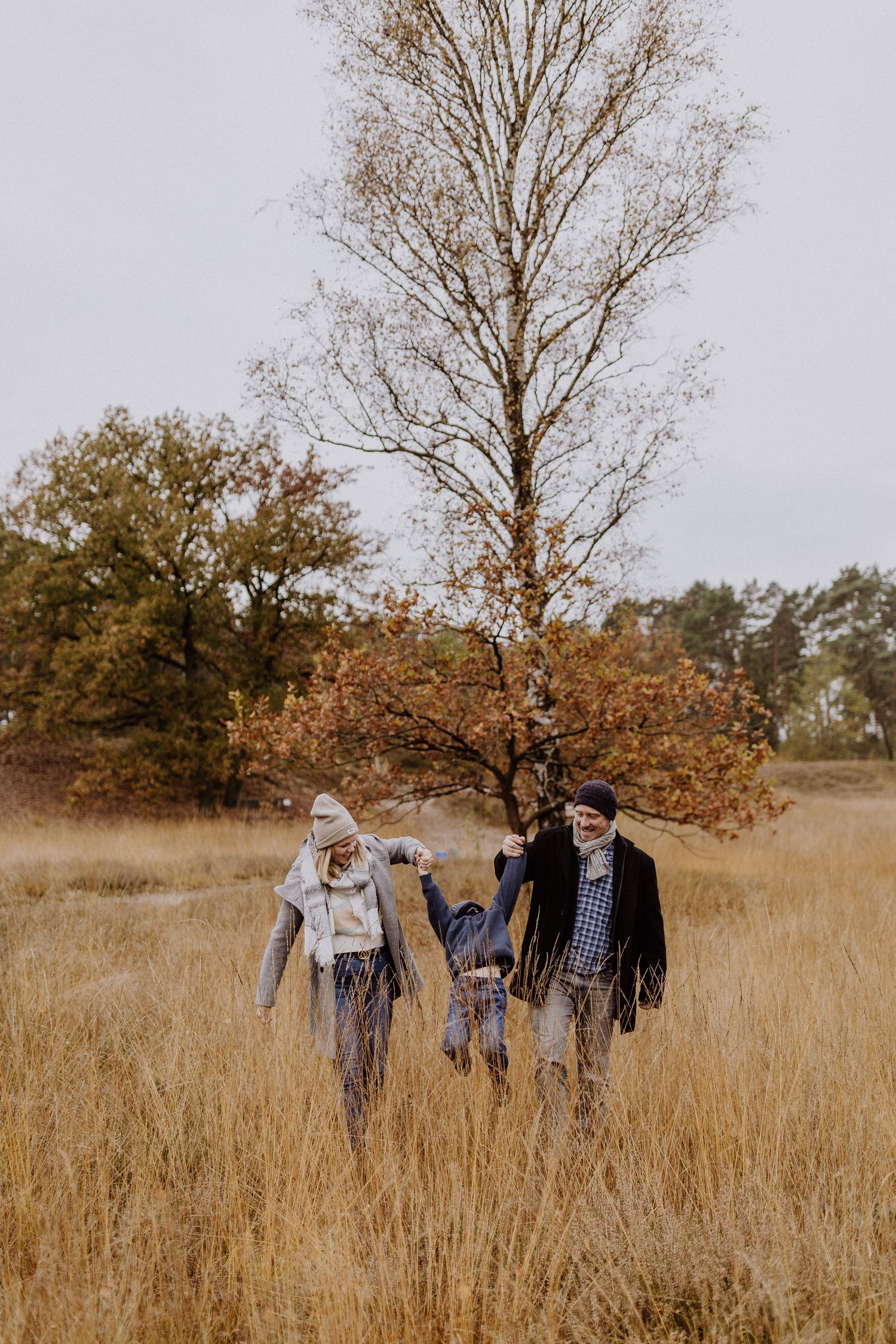 Familie geht gemeinsam durch das Herbstfeld mit hohem Gras und kahlen Bäumen.