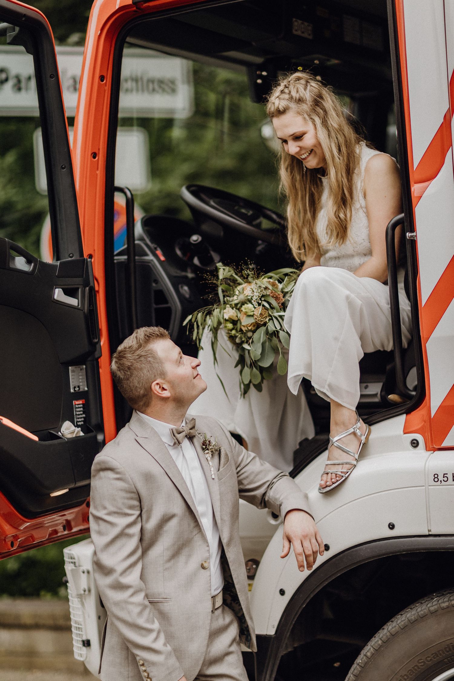 Braut im Hochzeitskleid sitzt in orangefarbenem Bauwagen, während der Bräutigam daneben kniet in Wolfsburg.