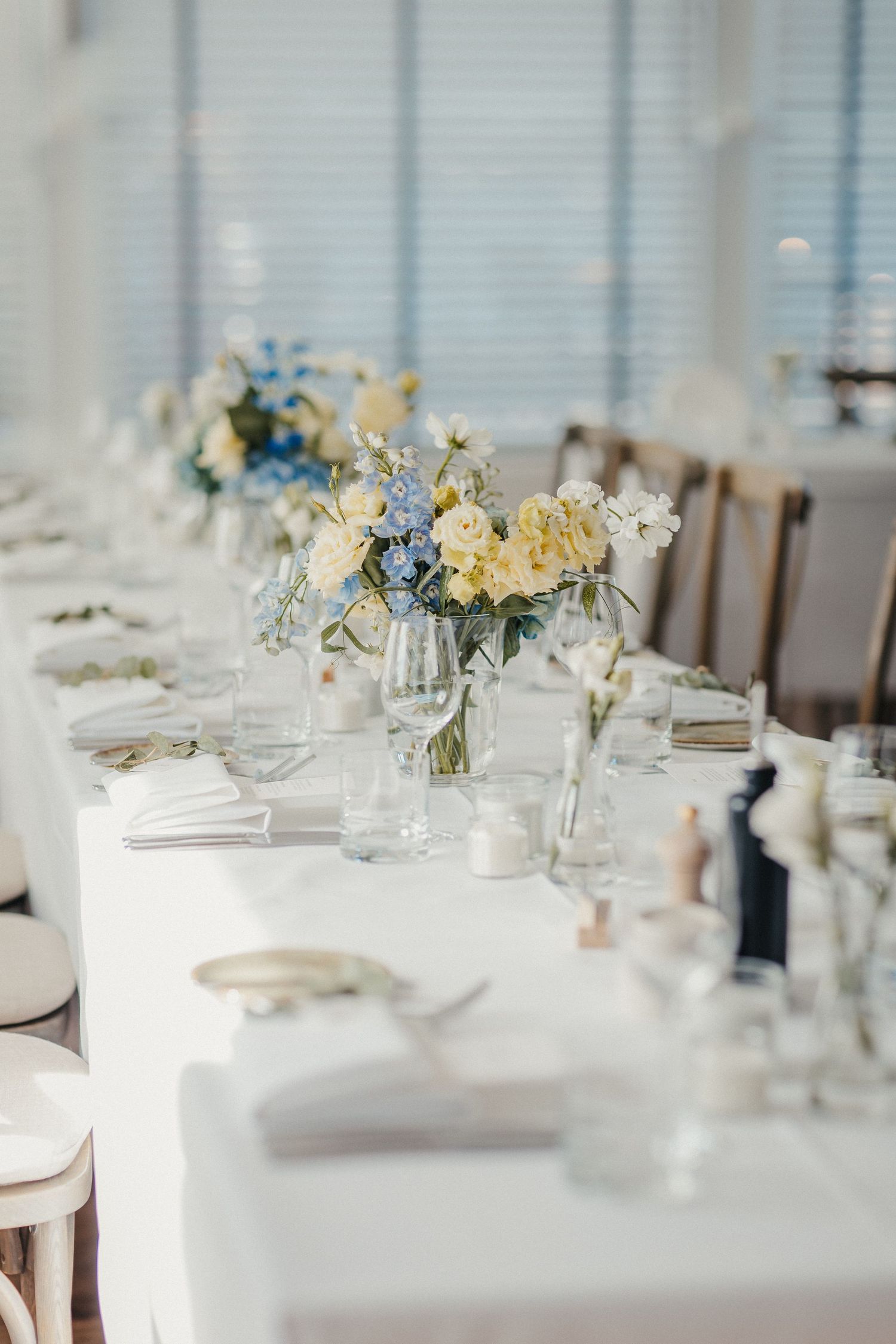 Eleganter Hochzeitsempfangstisch mit blauen und gelben floralen Mittelstücken auf weißer Bettwäsche.