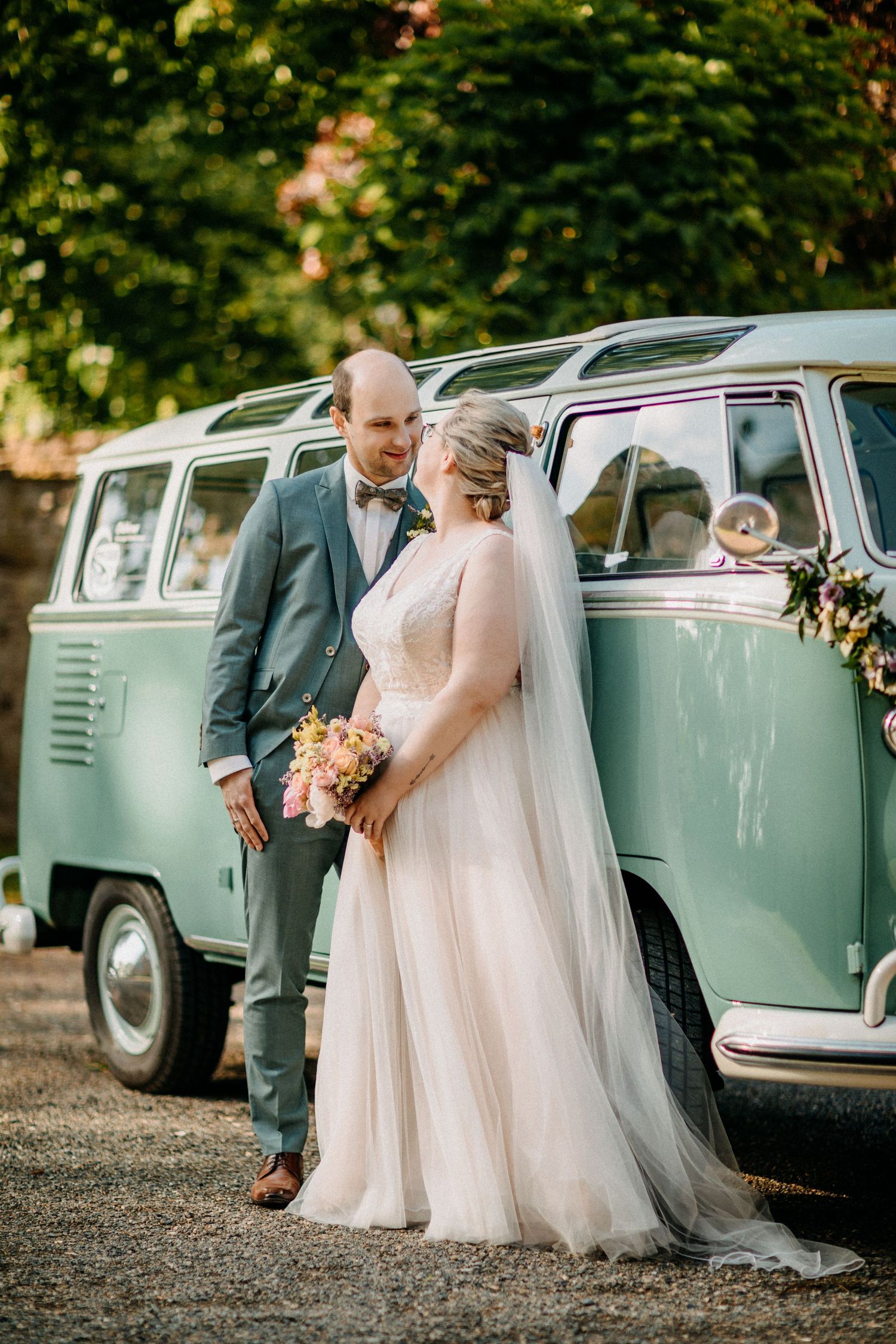 Ein Paar posiert an ihrem Hochzeitstag neben einem mintgrünen Vintage-VW-Bus.