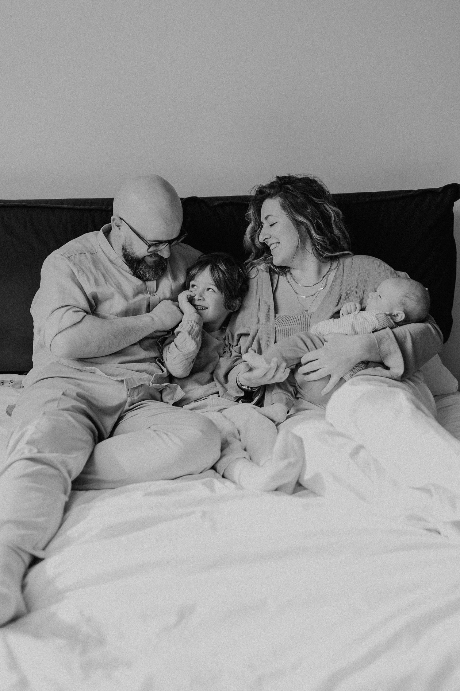 Familie entspannt sich gemeinsam auf dem Bett in lässigem Schwarz-Weiß-Porträt.