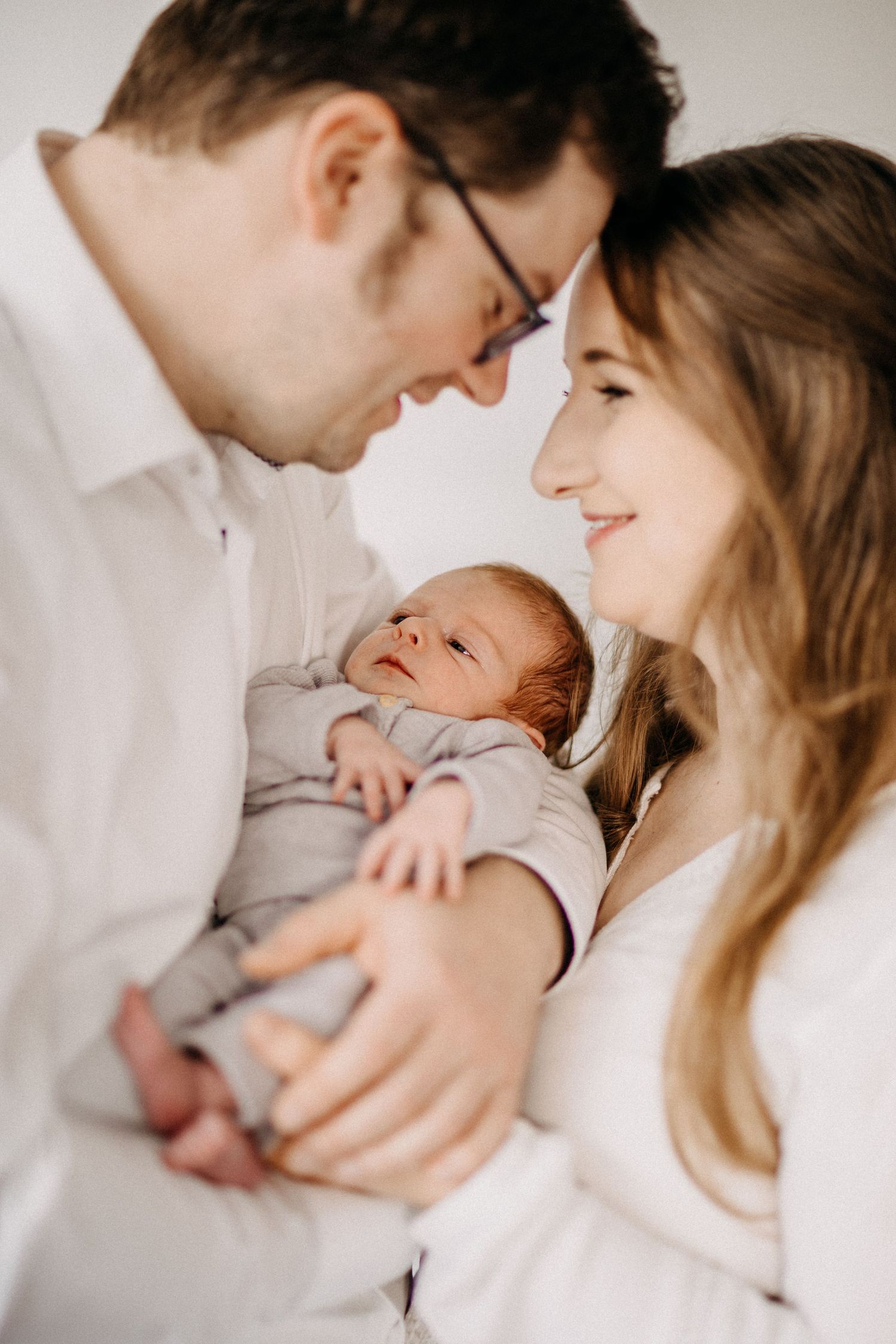 Intimer Familienmoment, während neue Eltern ihr neugeborenes Baby in weichem natürlichem Licht kuscheln.