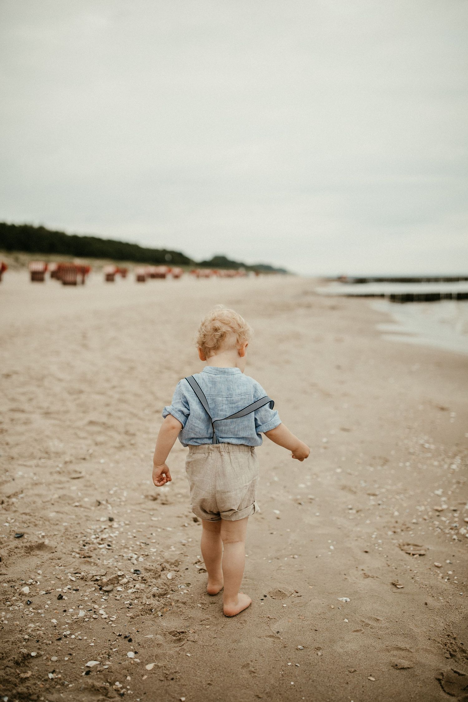 Kleines Kind geht barfuß am Strand mit blauem Hemd und Shorts.