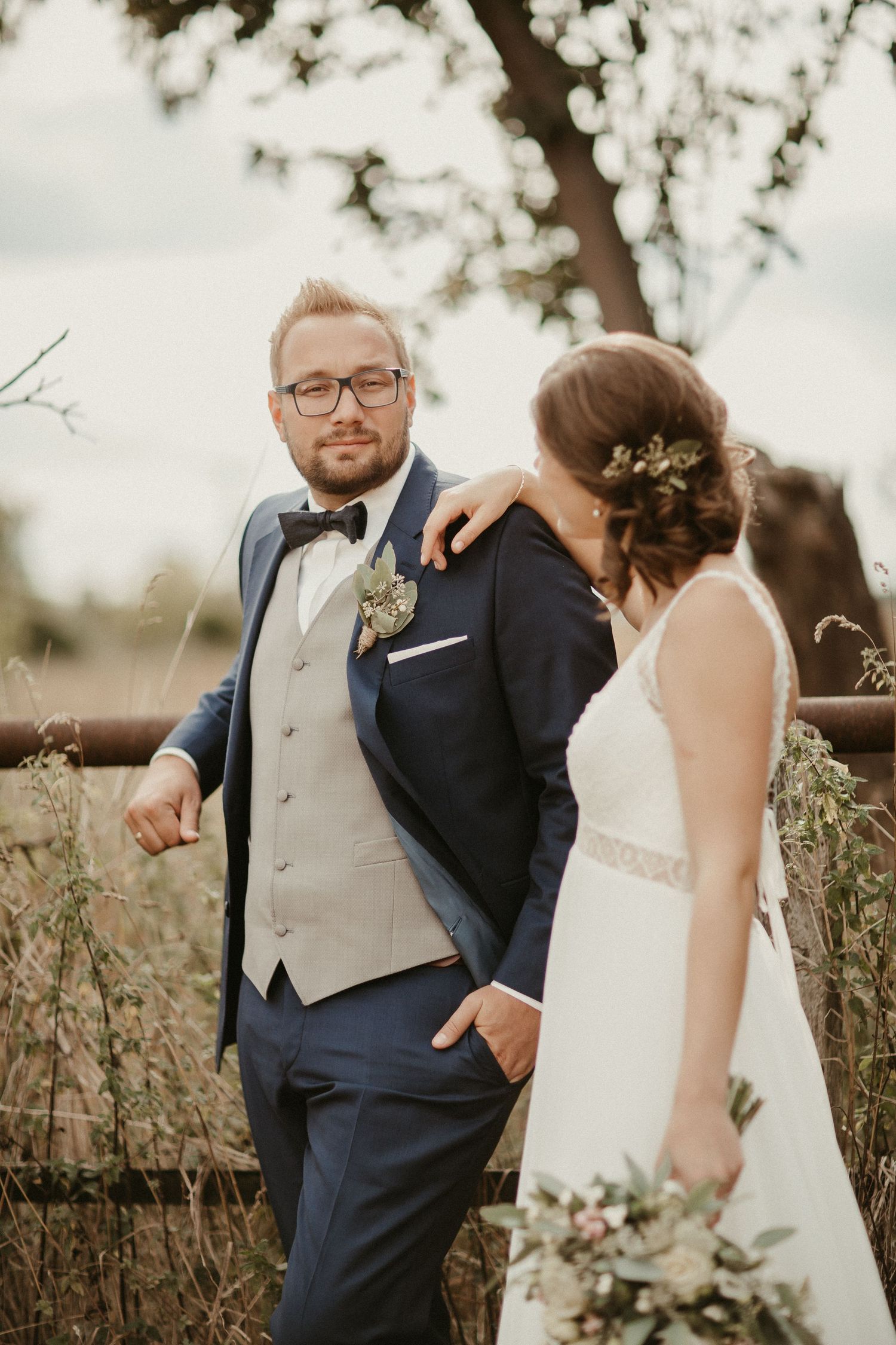 Romantisches Hochzeitsporträt eines Paares in formeller Kleidung, das auf dem Feld mit Bokeh-Hintergrund steht.