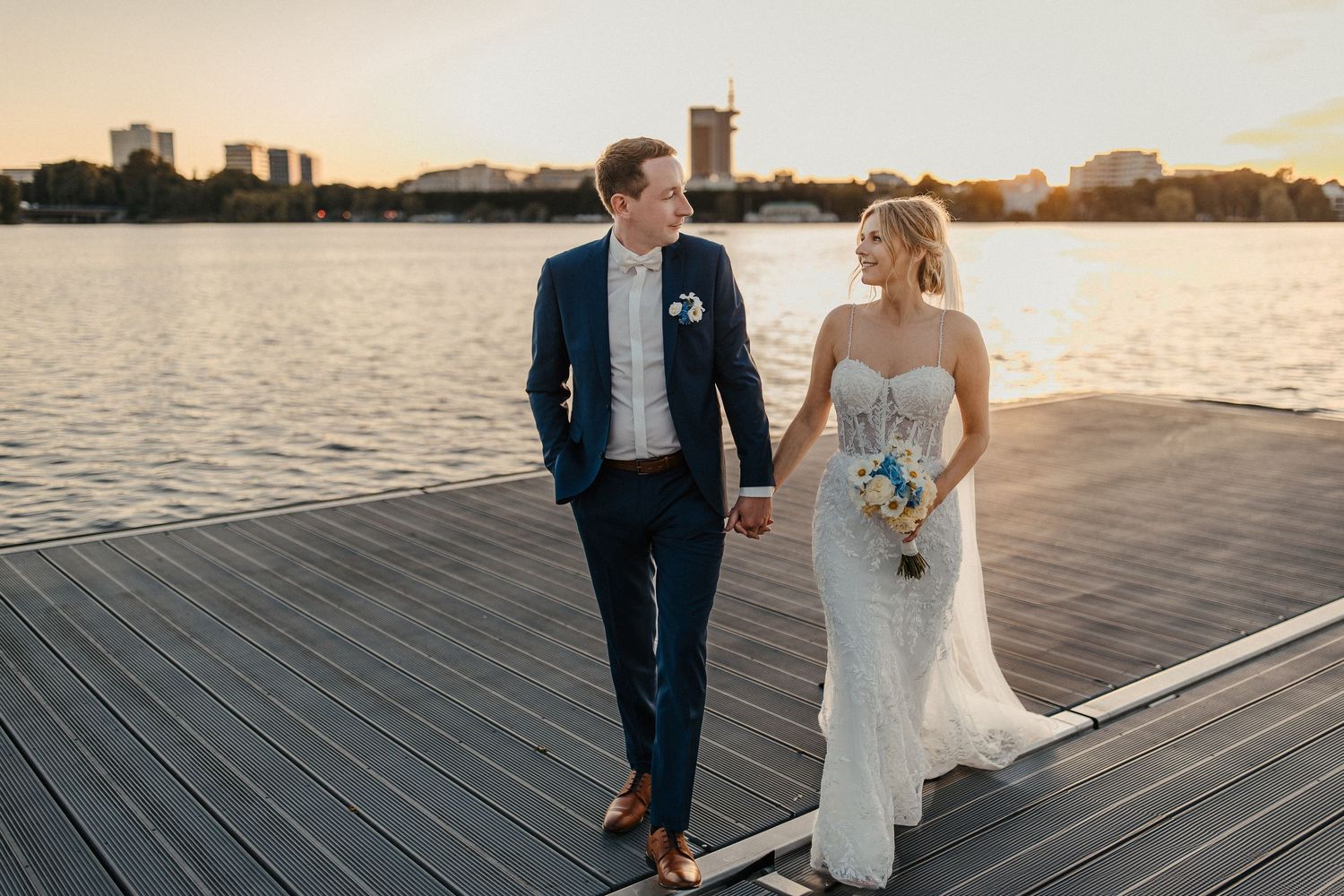 Jungvermählte gehen während der goldenen Stunde Hand in Hand auf der Promenade am Wasser in Hamburg an der Alster.