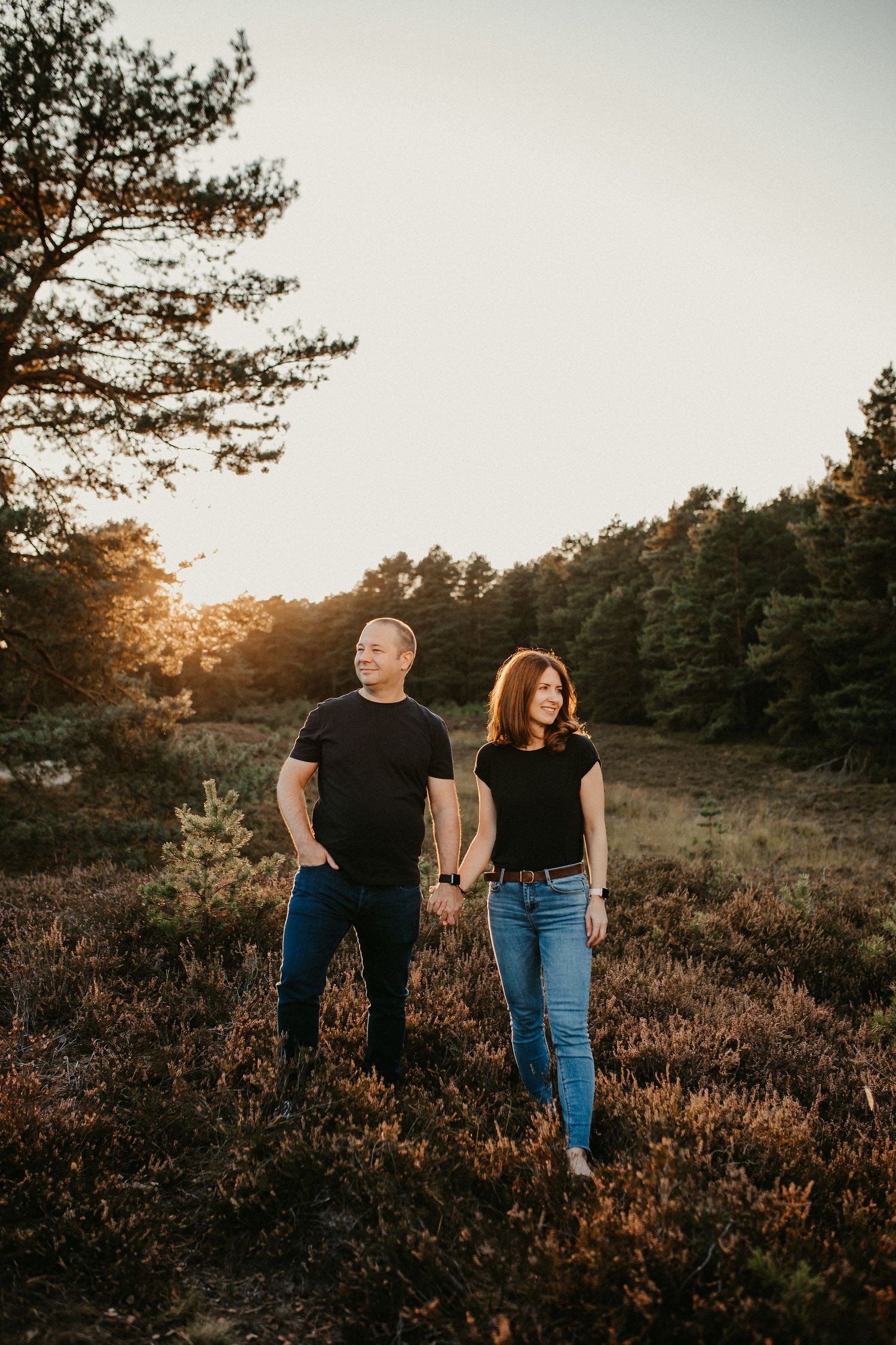 Zwei Personen in schwarzen Hemden und Jeans stehen zusammen auf einem Feld zur goldenen Stunde.