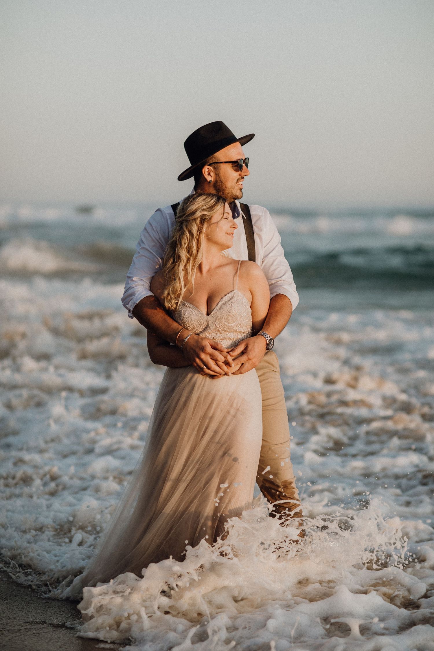 Romantisches Strandfotoshooting bei Sonnenuntergang mit fließendem Kleid, das Wellen fängt.