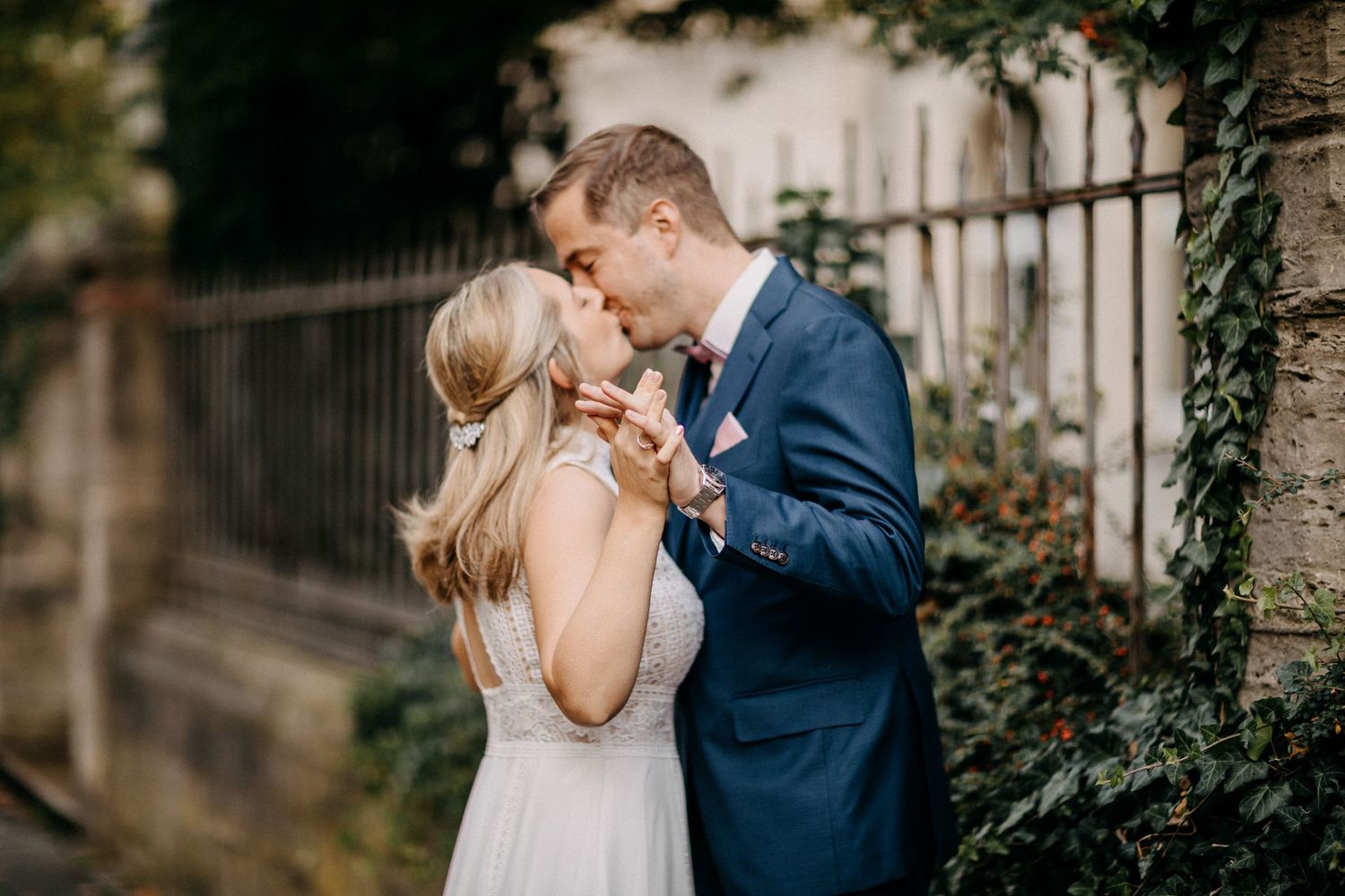 Ein romantisches Hochzeitspaar teilt einen zärtlichen Moment vor einer mit Efeu bedeckten Wand in der Abenddämmerung.