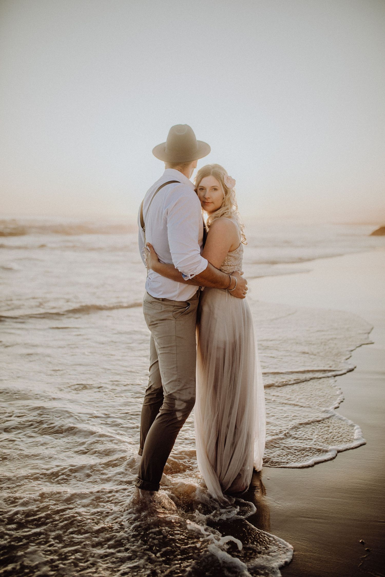 Paar in Hochzeitskleidung umarmt sich am Strand während der goldenen Stunde.