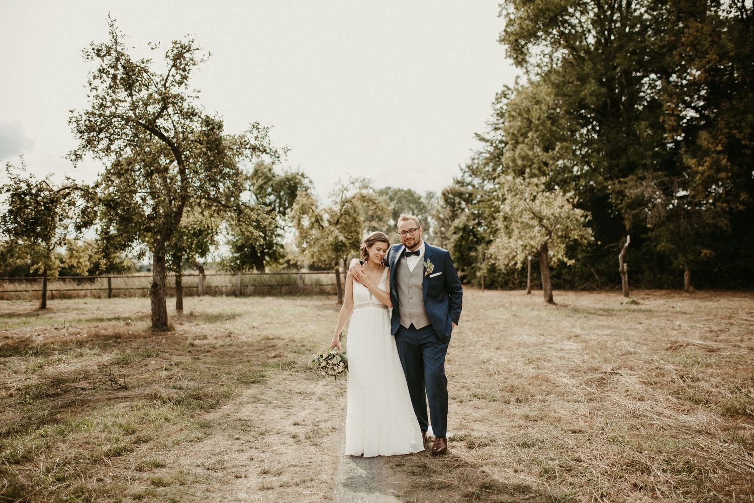 Hochzeitspaar steht zusammen in einer rustikalen Außenumgebung, umgeben von Herbstbäumen.