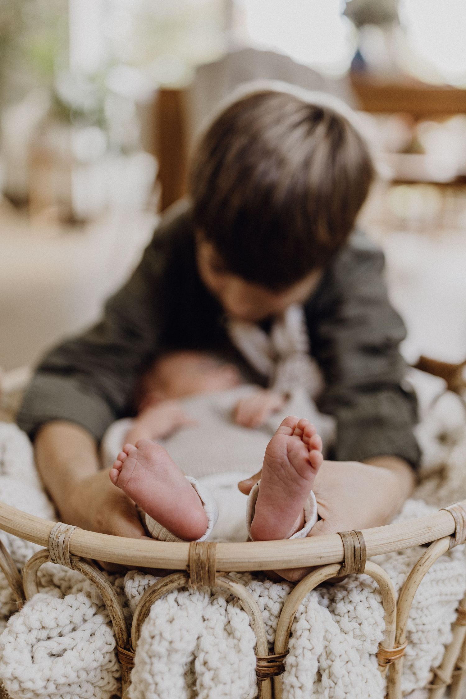 Nahaufnahme von winzigen Babyfüßen, während Bruder mit Säugling auf gewebtem Korb kuscheln.