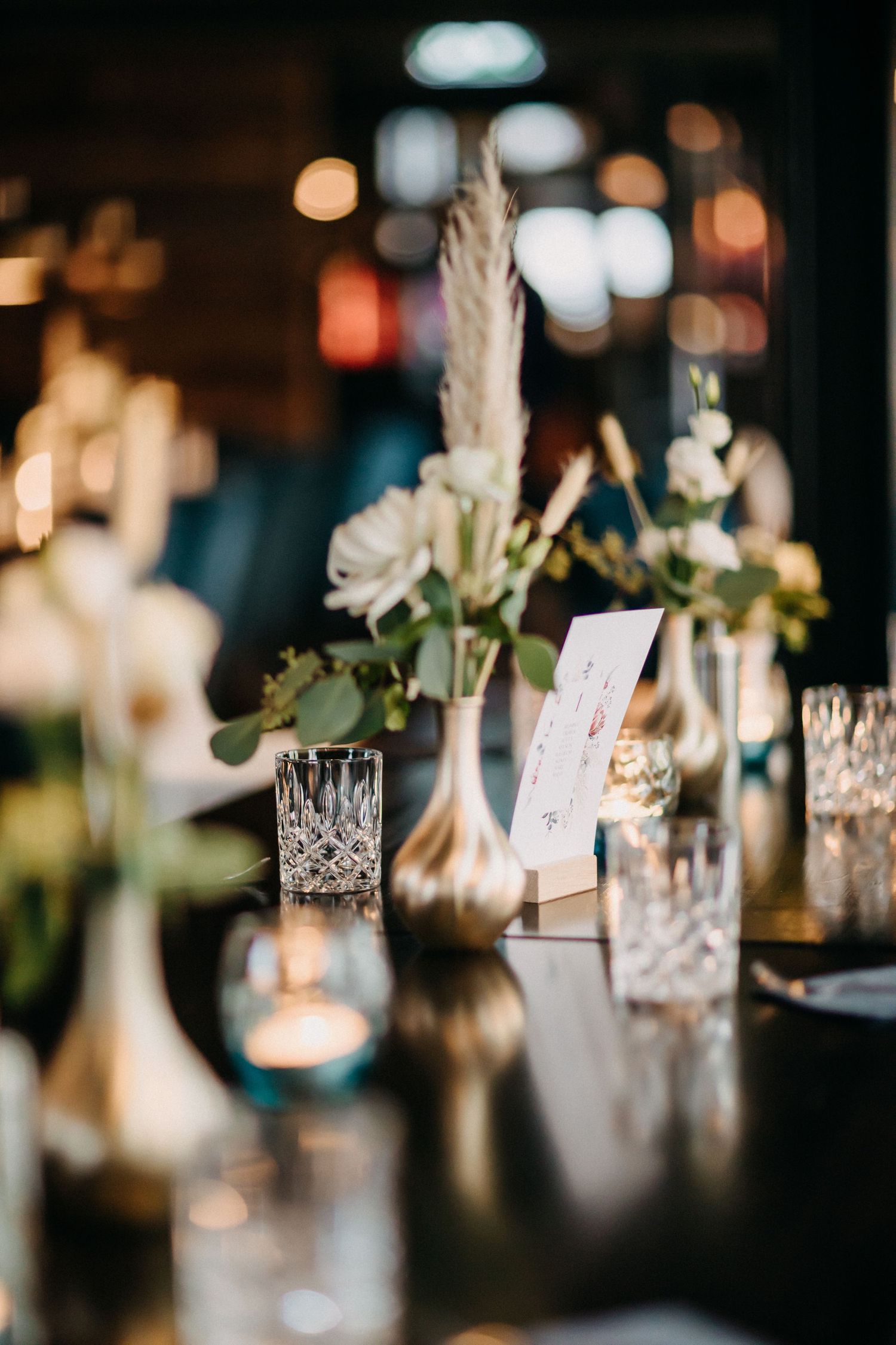 Elegante Hochzeitstischdekoration mit Kristallgläsern und weißen floralen Mittelstücken in stimmungsvoller Beleuchtung.