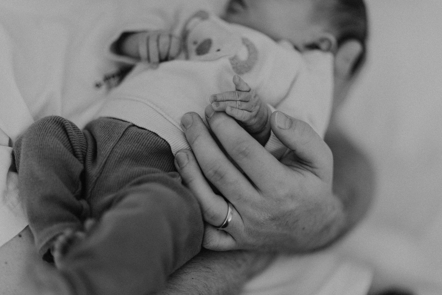 Schwarz-Weiß-Bild von winzigen Babyfüßen, die von fürsorglichen Händen gehalten werden.