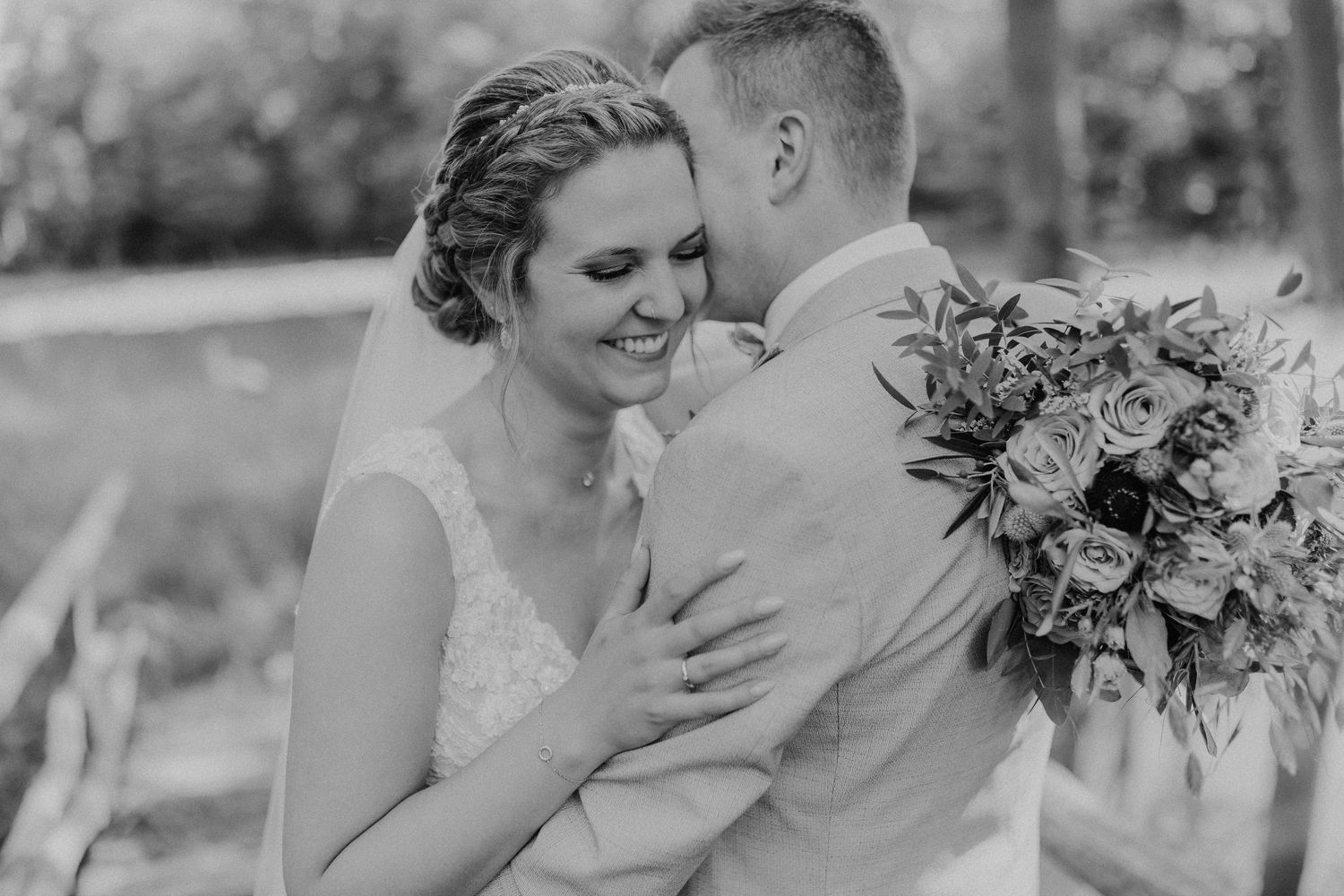 Schwarz-weißes Porträt eines romantischen Hochzeitspaares, das sich im Freien mit Blumenstrauß umarmt.