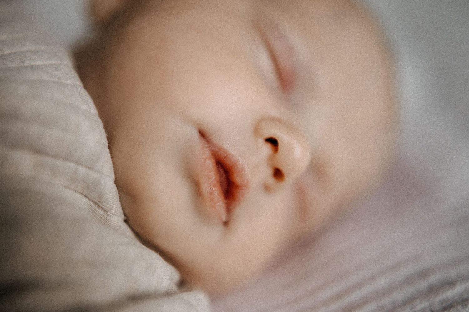 Friedliche Nahaufnahme des schlafenden Babygesichtes vor heller Bettwäsche.