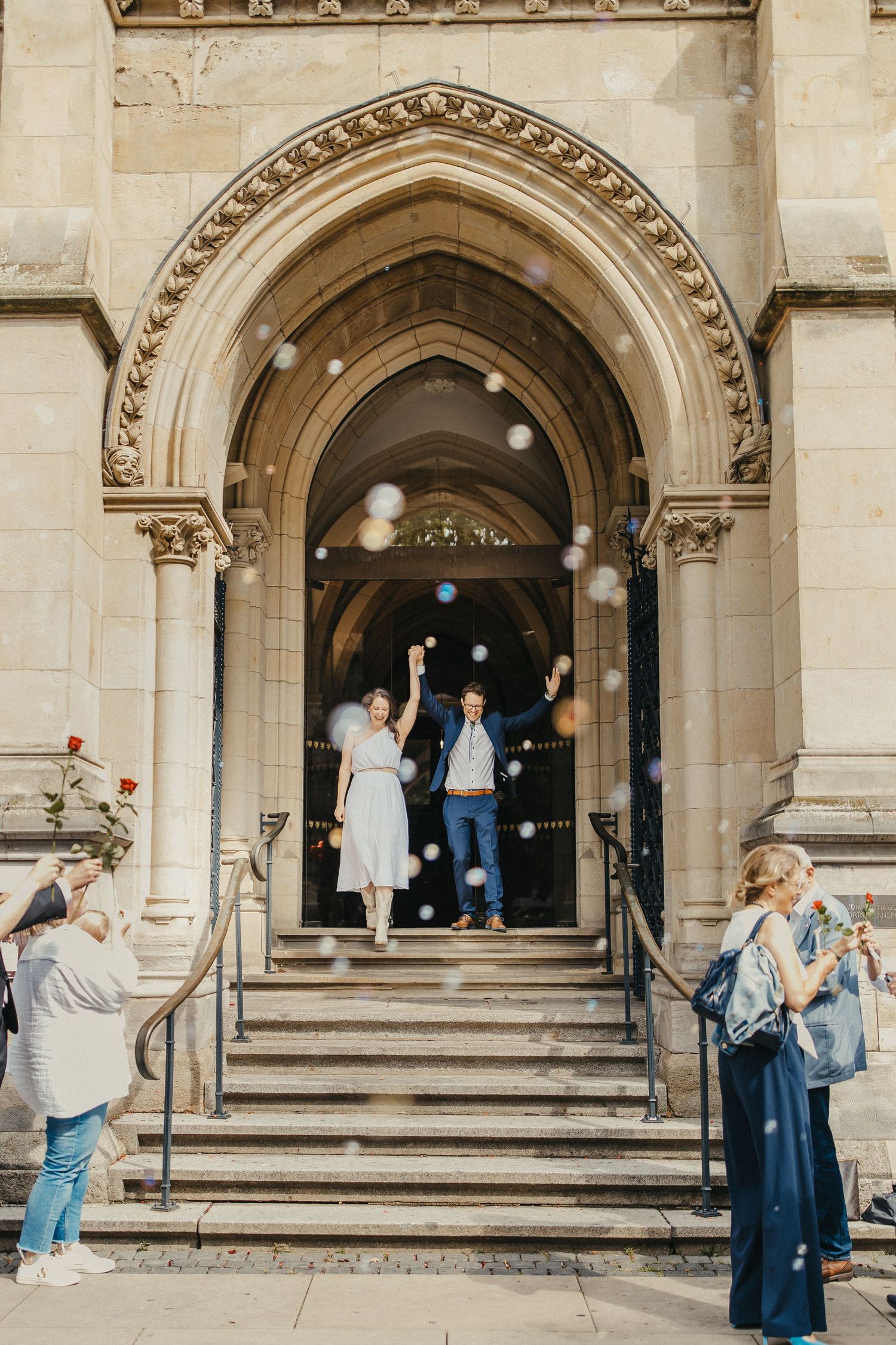 Hochzeitspaar verlässt historische Steinkirche, während Gäste Konfetti auf Stufen werfen.