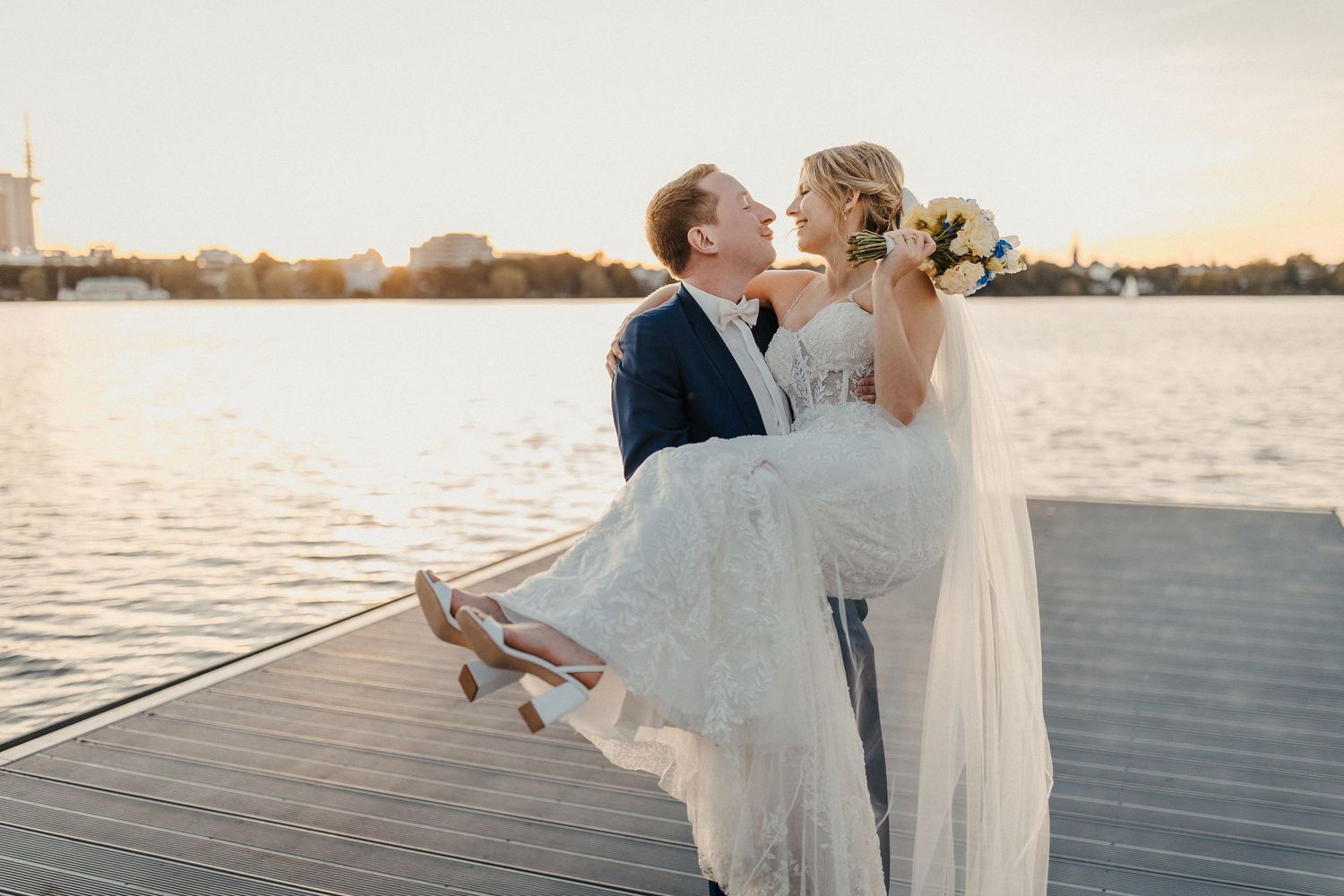 Bräutigam hebt Braut in weißem Kleid während Sonnenuntergang Fotoshooting am Wasser Dock in Hamburg an der Alster.
