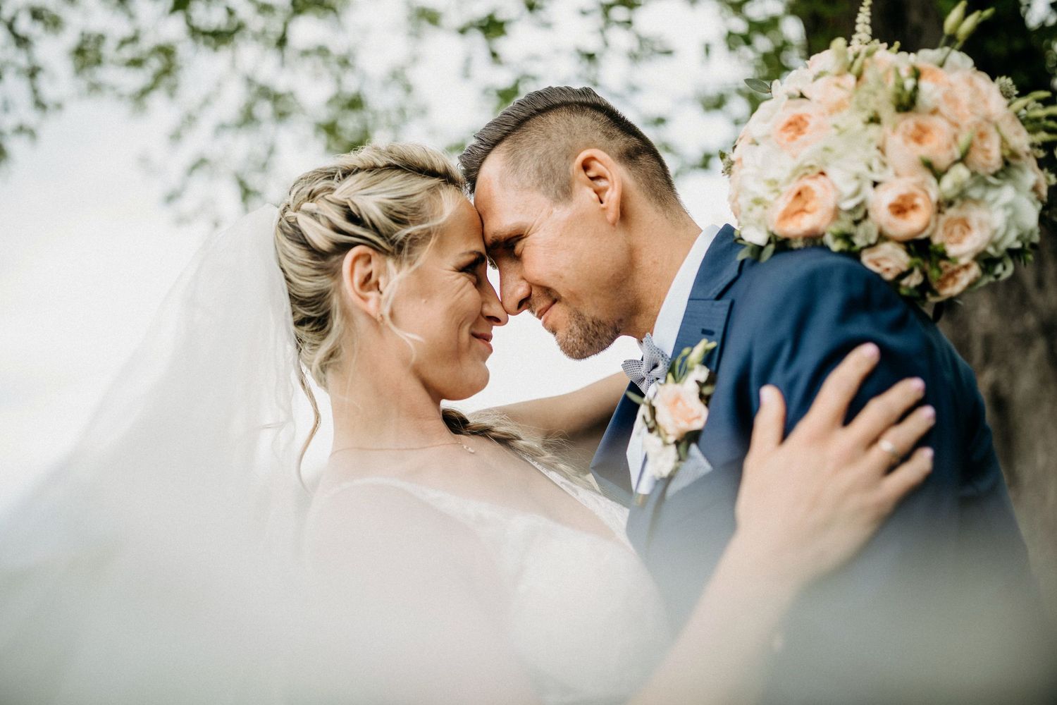 Romantischer Hochzeitsmoment mit Pfirsichstrauß und marineblauem Anzug bei einer Gartenzeremonie im Freien.