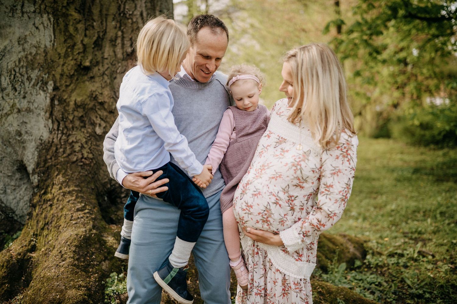 Familienfotoshooting im Freien mit Eltern und kleinen Kindern an einem großen Baumstamm.