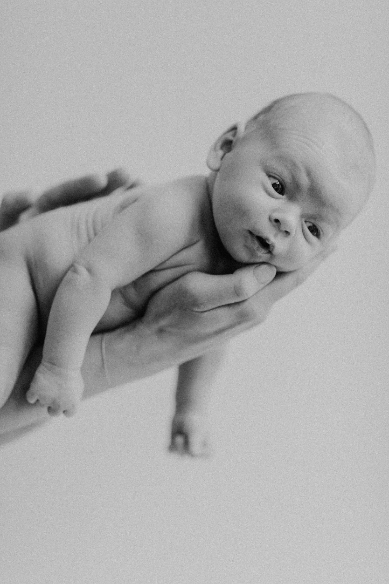 Ein neugeborenes Baby liegt auf der Seite vor weißem Hintergrund in Schwarz-Weiß-Fotografie.