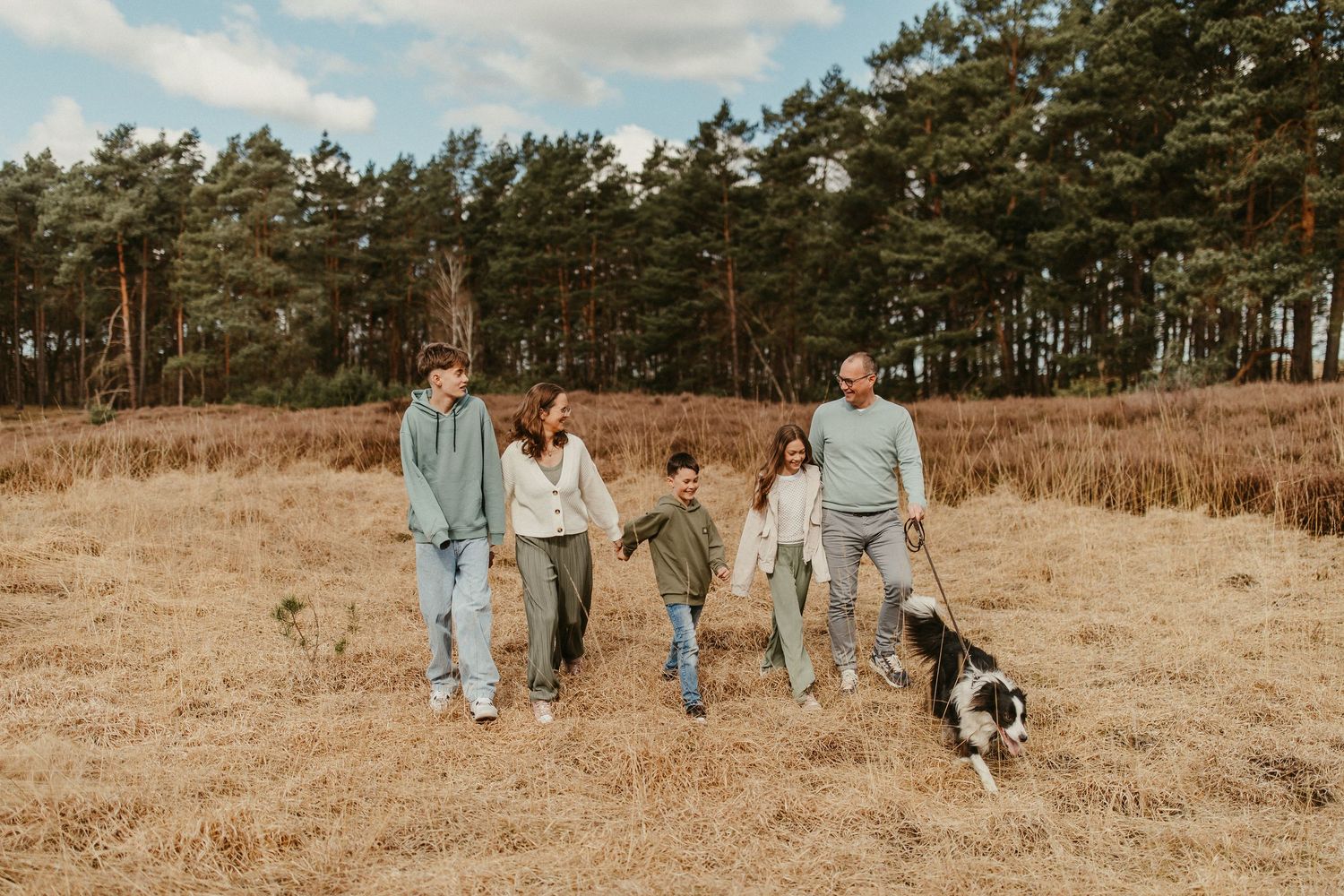 Familie geht mit Hund durch Feld in der Nähe von Kiefernwald.