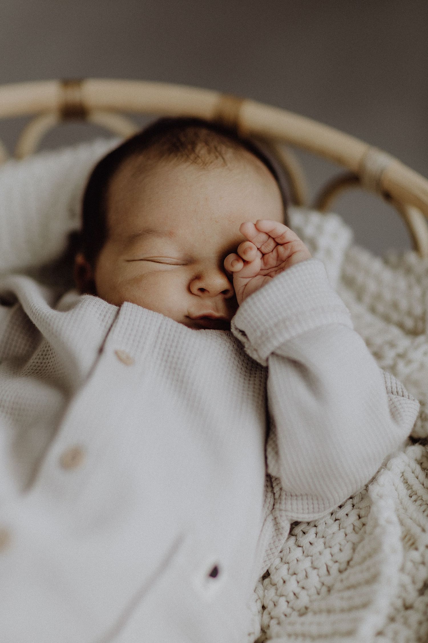 Schlafendes Kleinkind in weißem Strampler, das sich die Augen reibt, während es sich in einer kuscheligen Strickdecke ausruht.