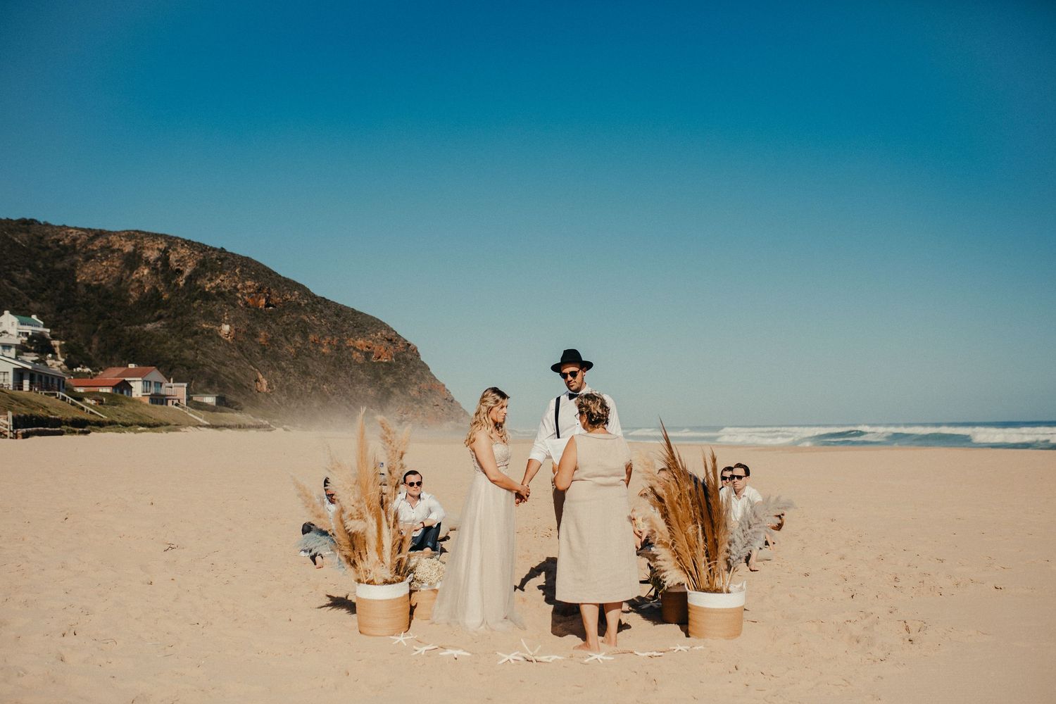 Paar feiert ihre Strandhochzeit mit getrockneten Palmwedeln an einem sonnigen Tag.