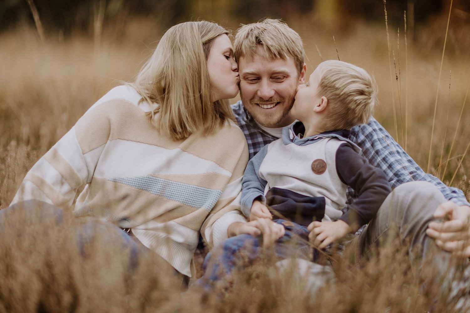 Eine Familie teilt zärtliche Momente, während sie gemeinsam im hohen Herbstgras sitzt.