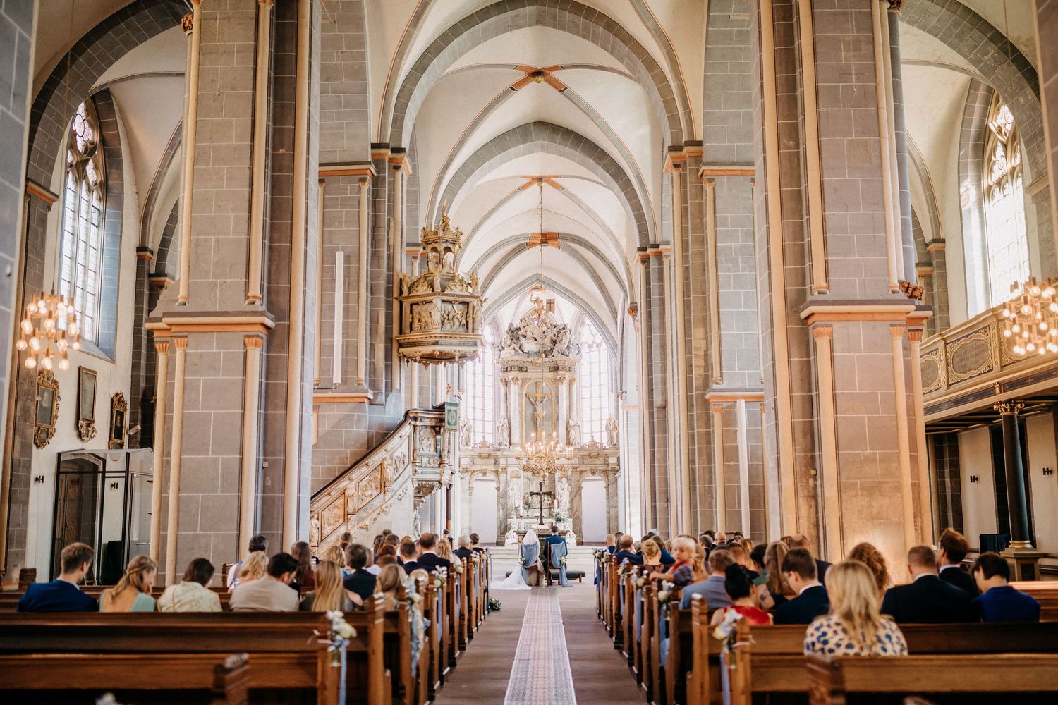Innenraum einer großen Kathedrale mit gewölbten Decken und Reihen von Bänken während einer Hochzeitszeremonie.