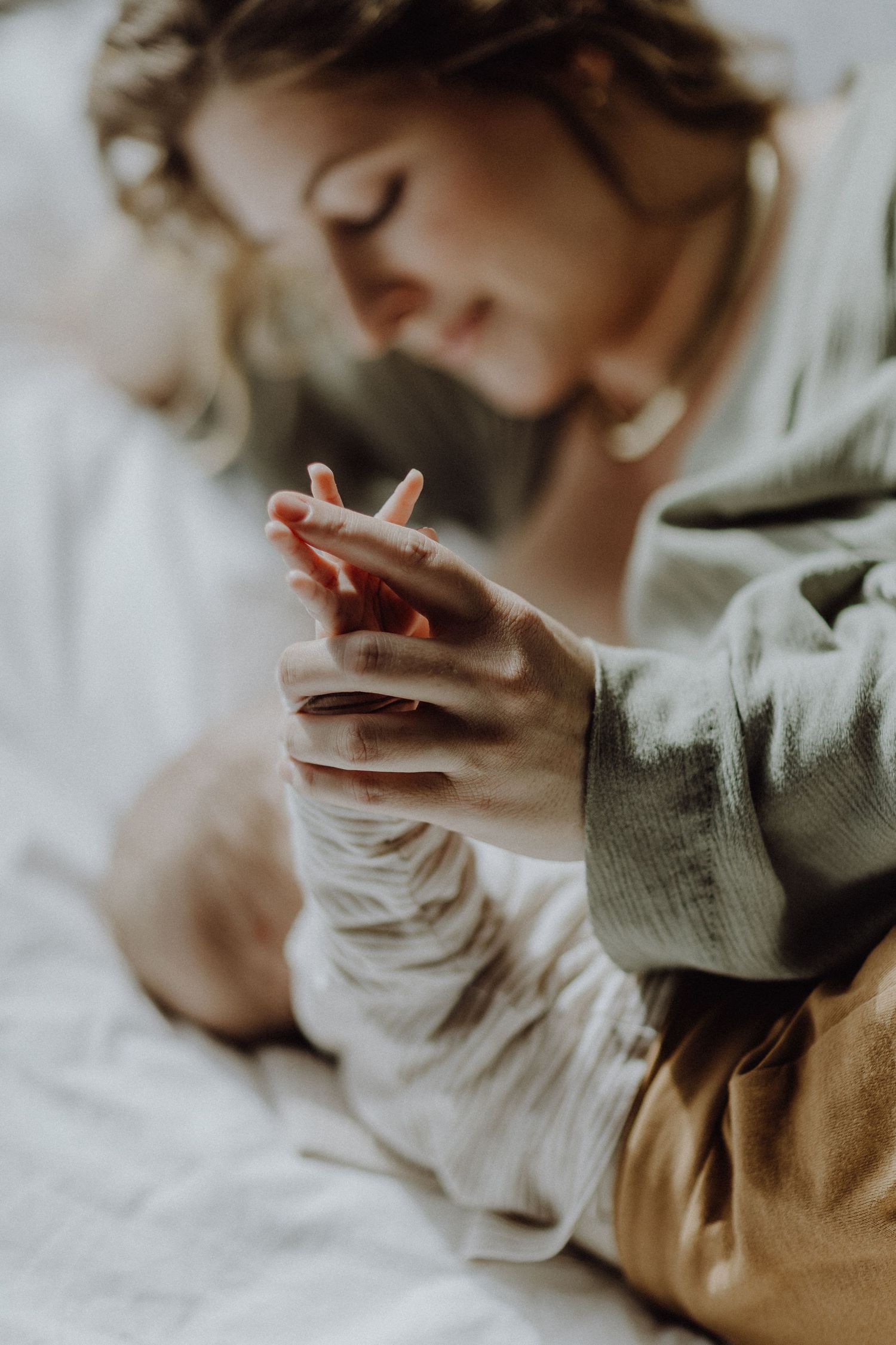 Nahaufnahme von Händen, die sich berühren, während das Baby im weichen Licht ruht.