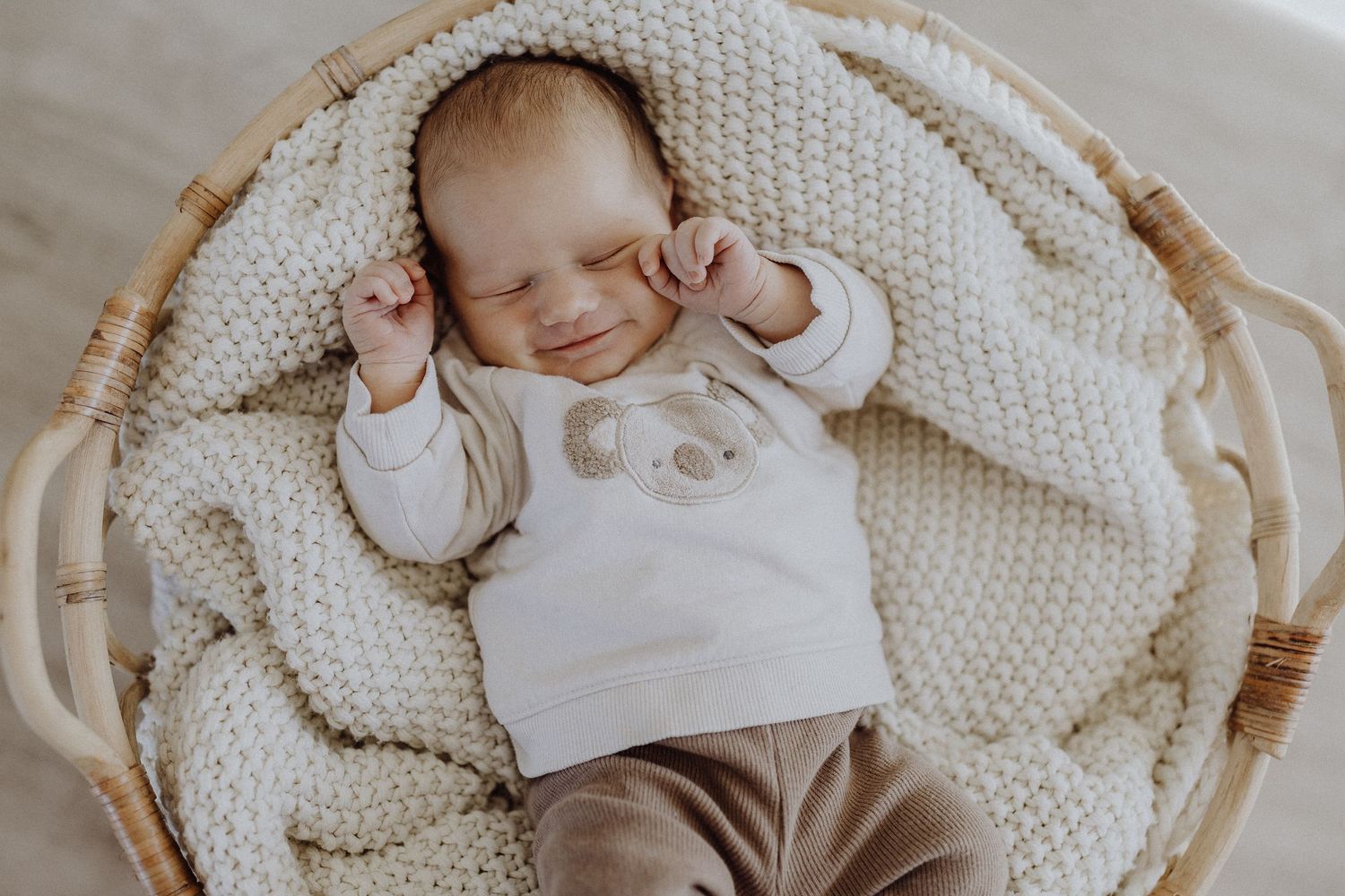 Schlafendes Baby in weißem Outfit liegt in gewebtem Korb auf Strickdecke in Wolfsburg.