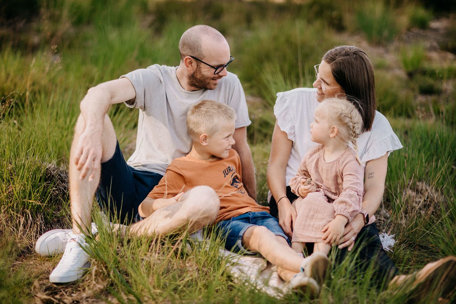 Die vierköpfige Familie sitzt während des Fotoshootings im Freien in Freizeitkleidung zusammen auf Gras.