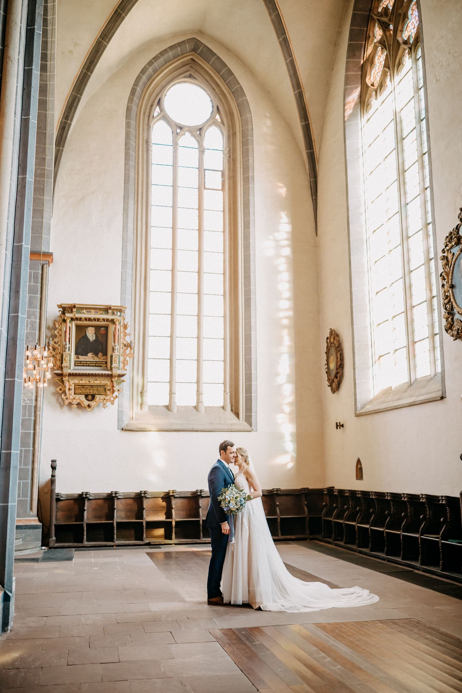 Ein Paar umarmt sich in einer großen Kathedrale mit hoch aufgehenden gotischen gewölbten Fenstern und kunstvollen architektonischen Details.