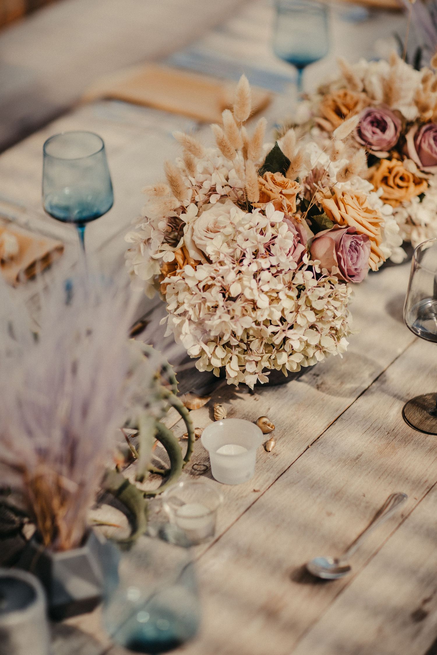 Rustikale Hochzeitstischdekoration mit getrockneten Blumen und blauen Glaswaren.