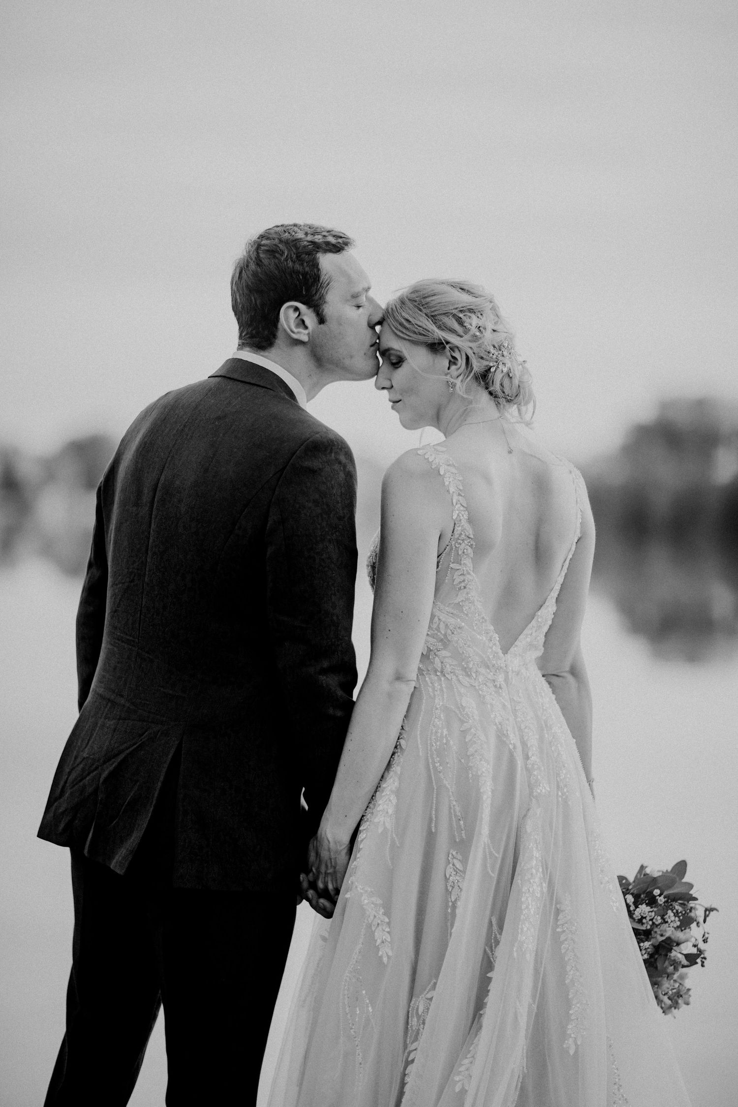 Ein schwarz-weißes romantisches Hochzeitsporträt, aufgenommen von einem See mit Spitzenkleiddetails.