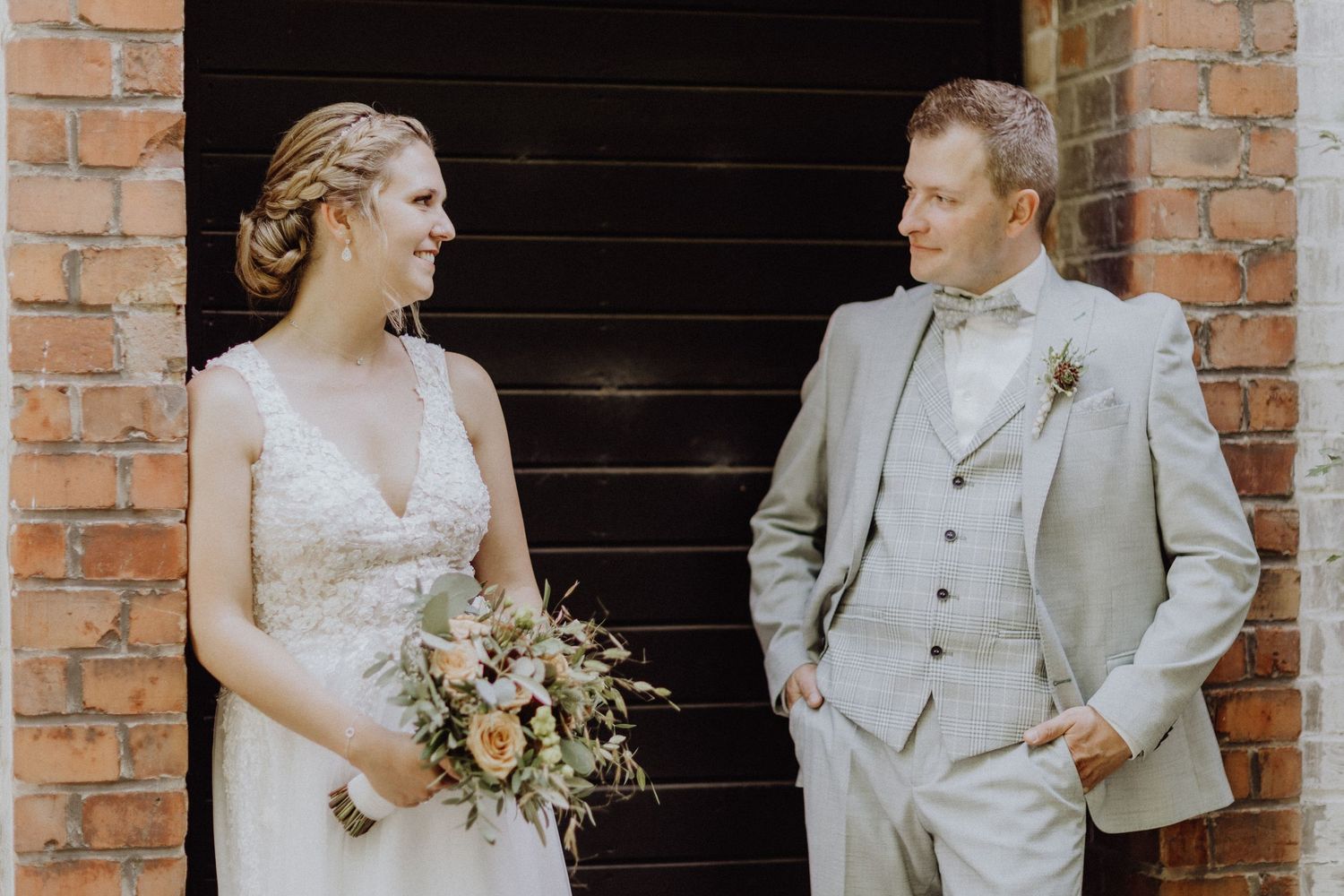 Hochzeitspaar teilt einen freudigen Moment vor einem rustikalen Backsteinmauerhintergrund in Gifhorn.