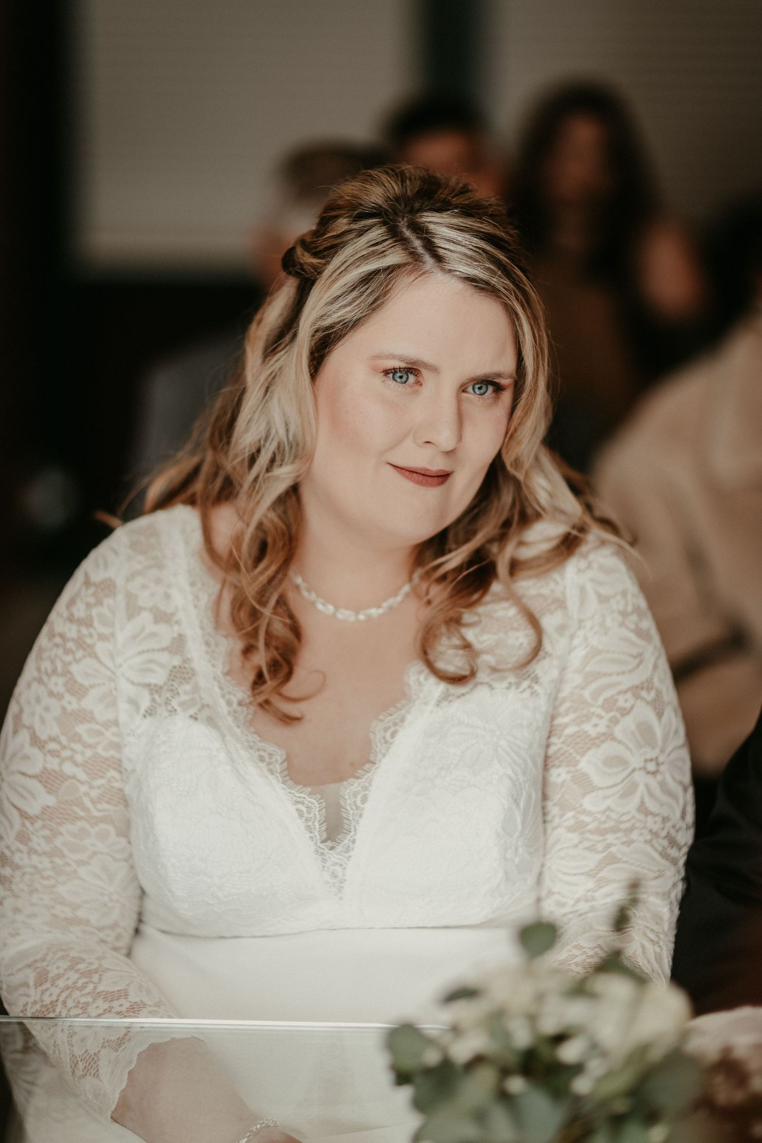 Braut in eleganter Spitze Langarm Brautkleid mit Perlenkette sitzt am Empfangstisch.