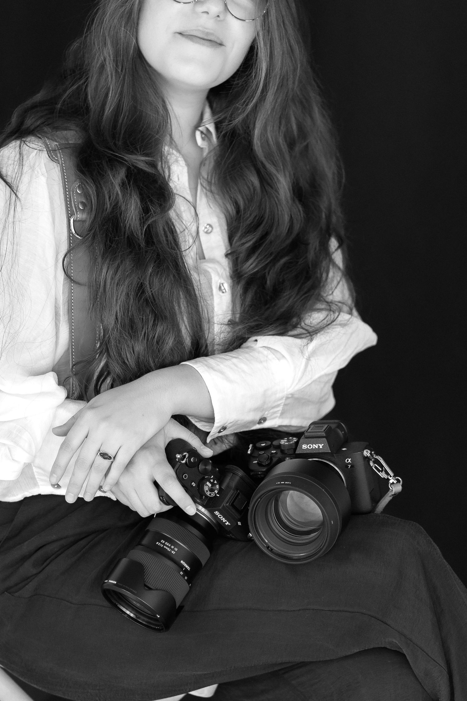 Black and white portrait of a photographer wearing a white button-up shirt while holding a professional camera with lens.