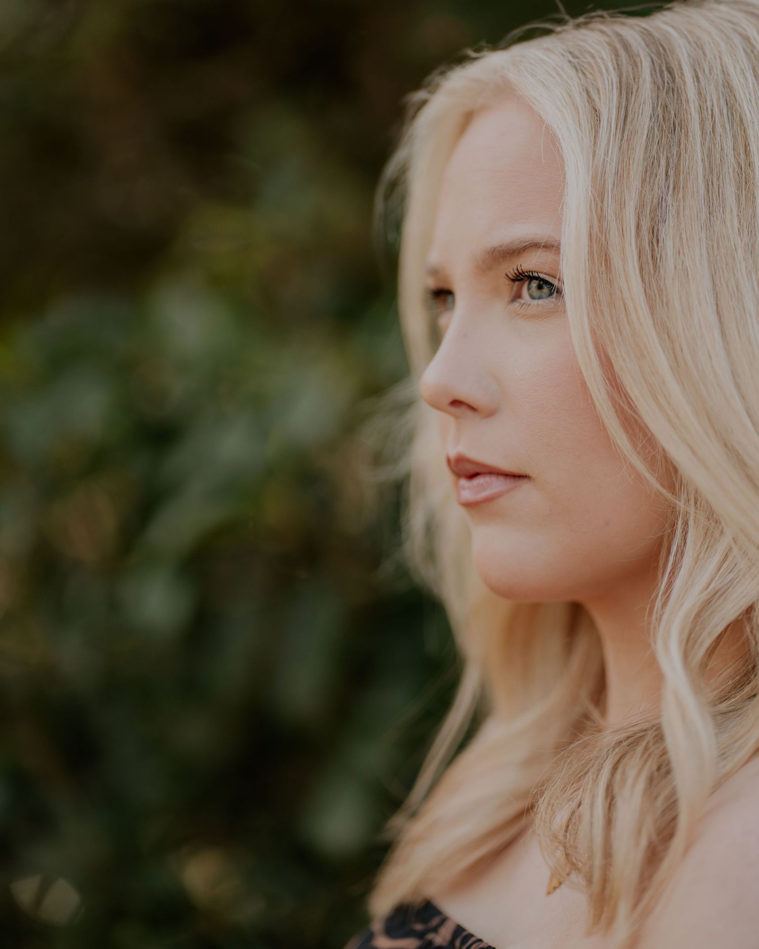 A woman with blonde wavy hair gazes thoughtfully against a soft natural background in golden light.