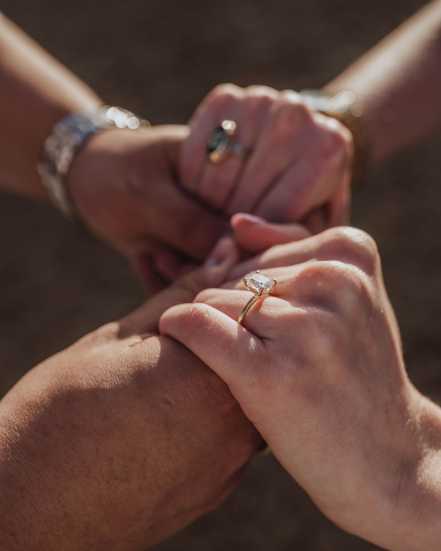 Two hands lovingly clasped together, with engagement rings glinting in warm sunlight, symbolizing commitment and unity.