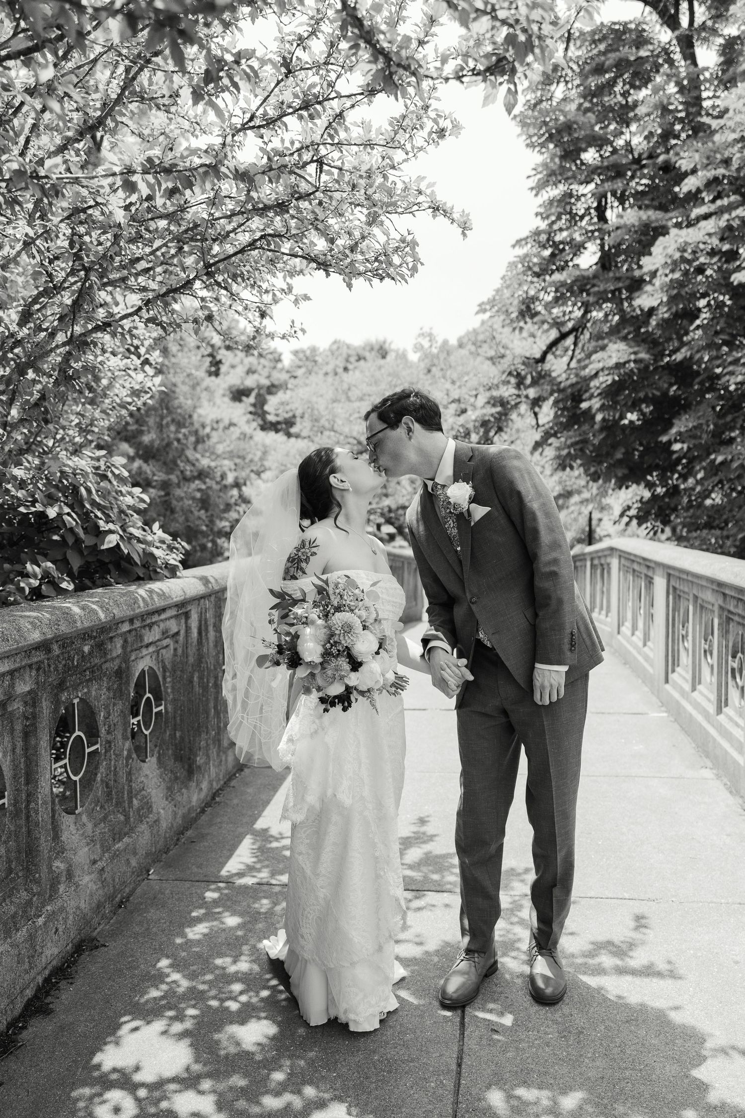 A couple in wedding attire walks together along a sun-dappled stone bridge pathway during their wedding. Cincinnati Wedding Photography