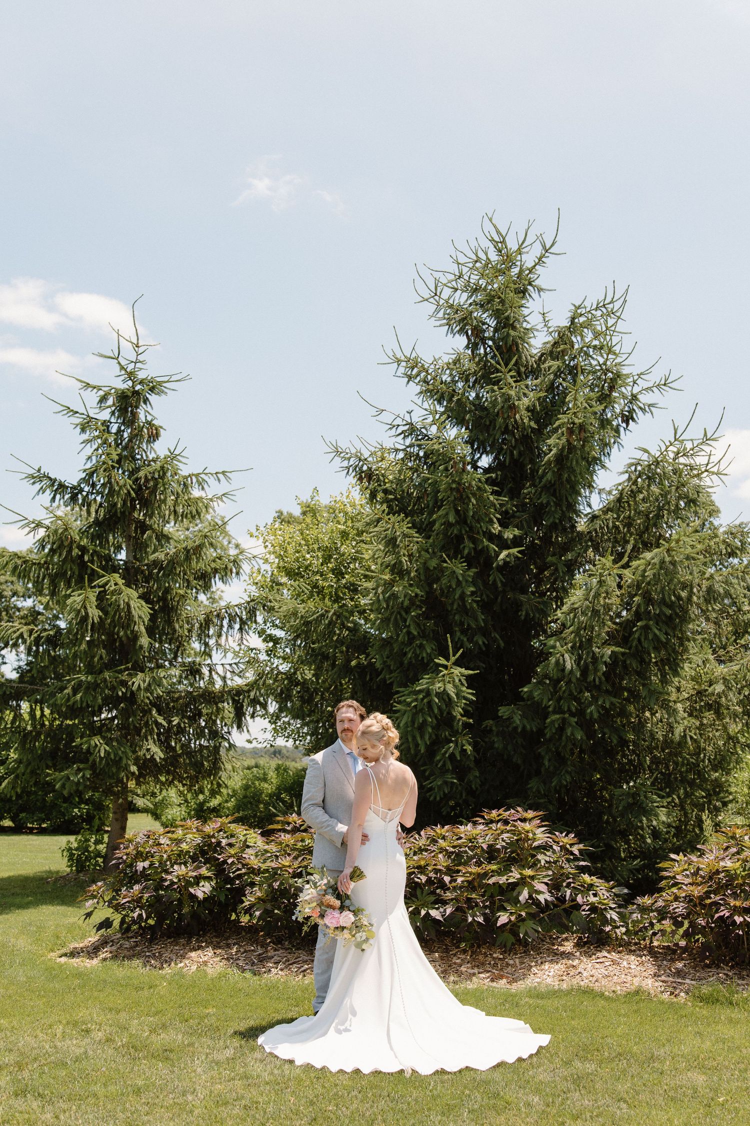 A romantic outdoor wedding moment captured in a series of five photos showing a couple among evergreen trees and gardens.