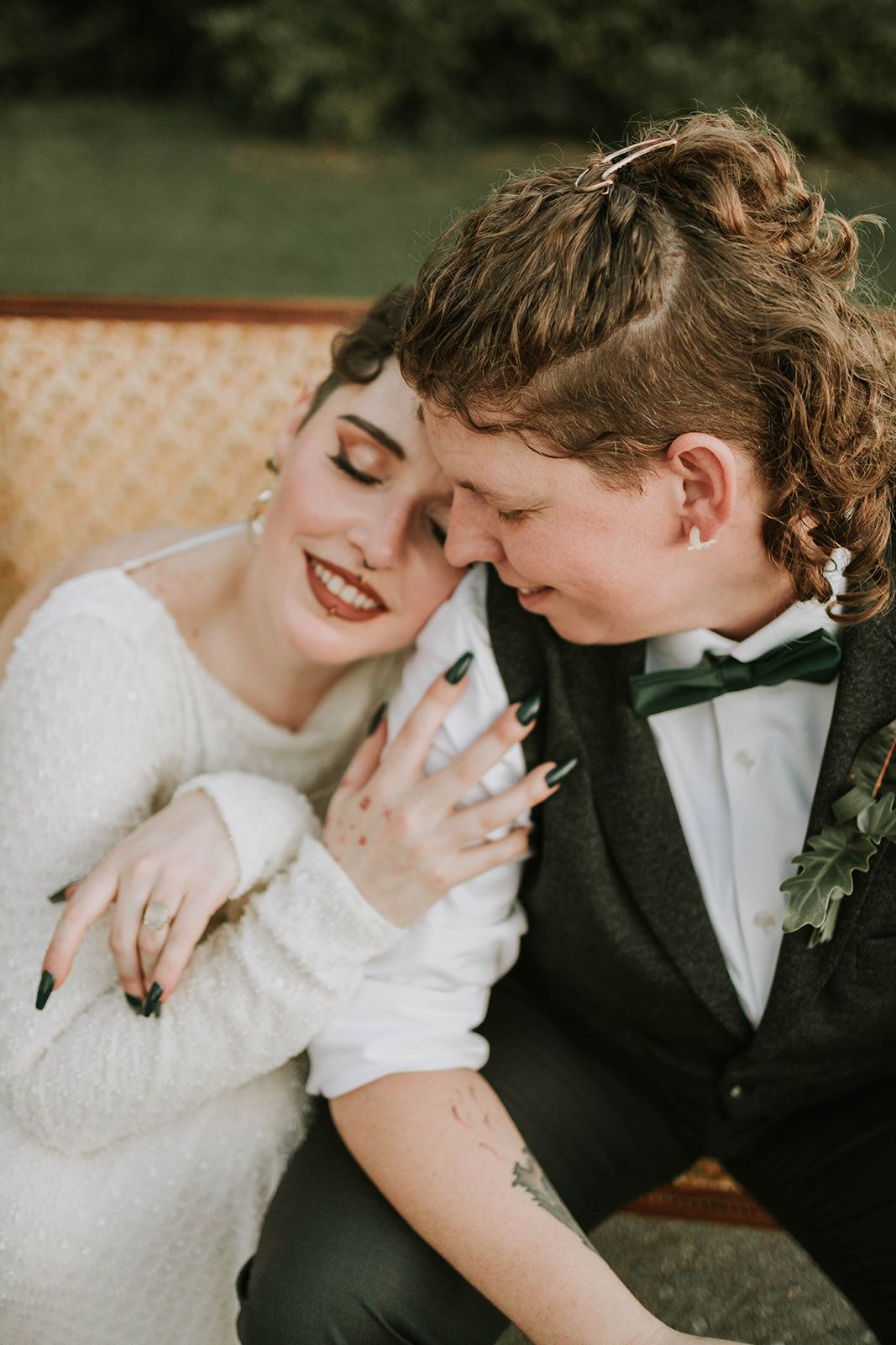 A newlywed couple in wedding attire shares an intimate moment on a vintage couch during their outdoor celebration.