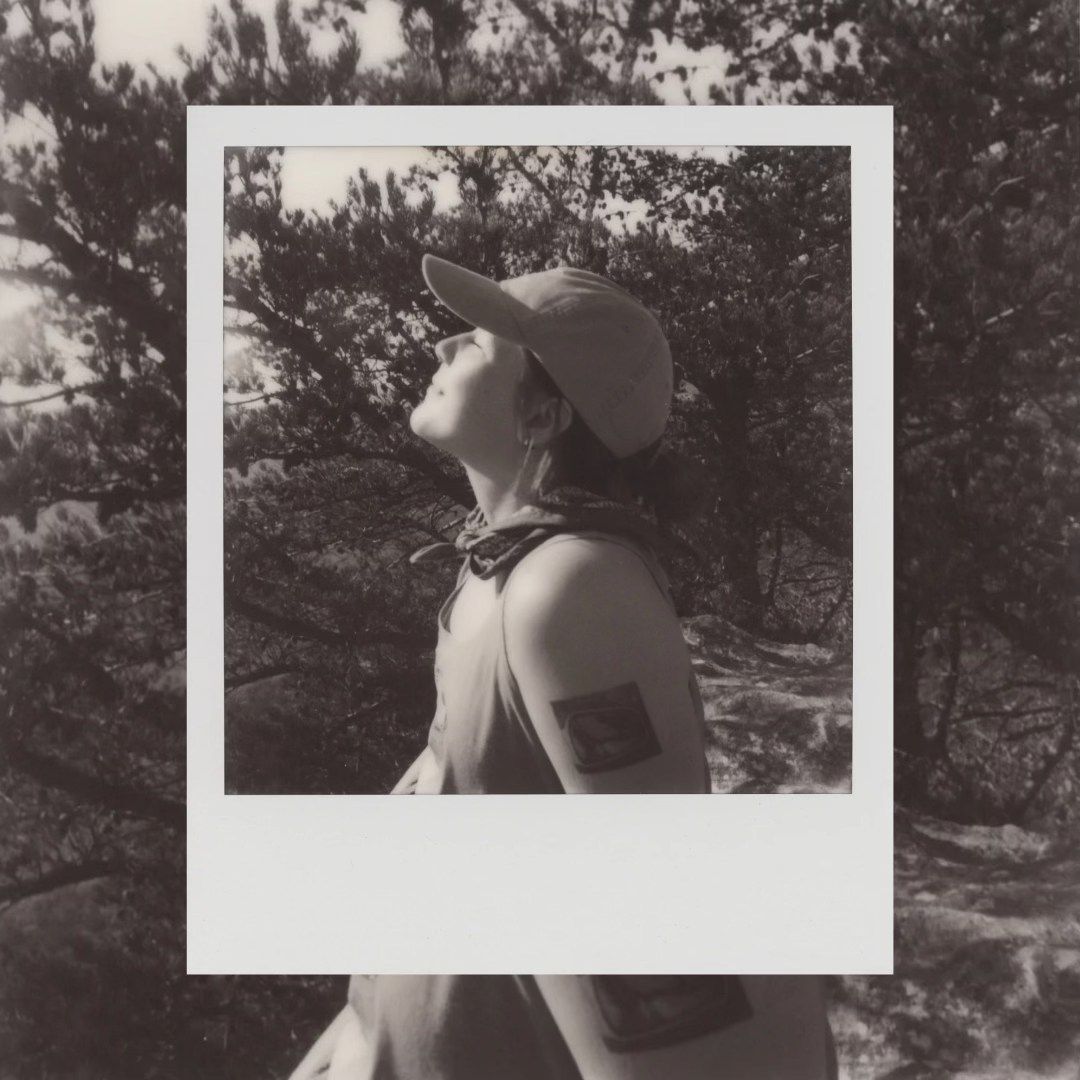 Black and white Polaroid photograph showing a silhouette wearing a baseball cap in nature.